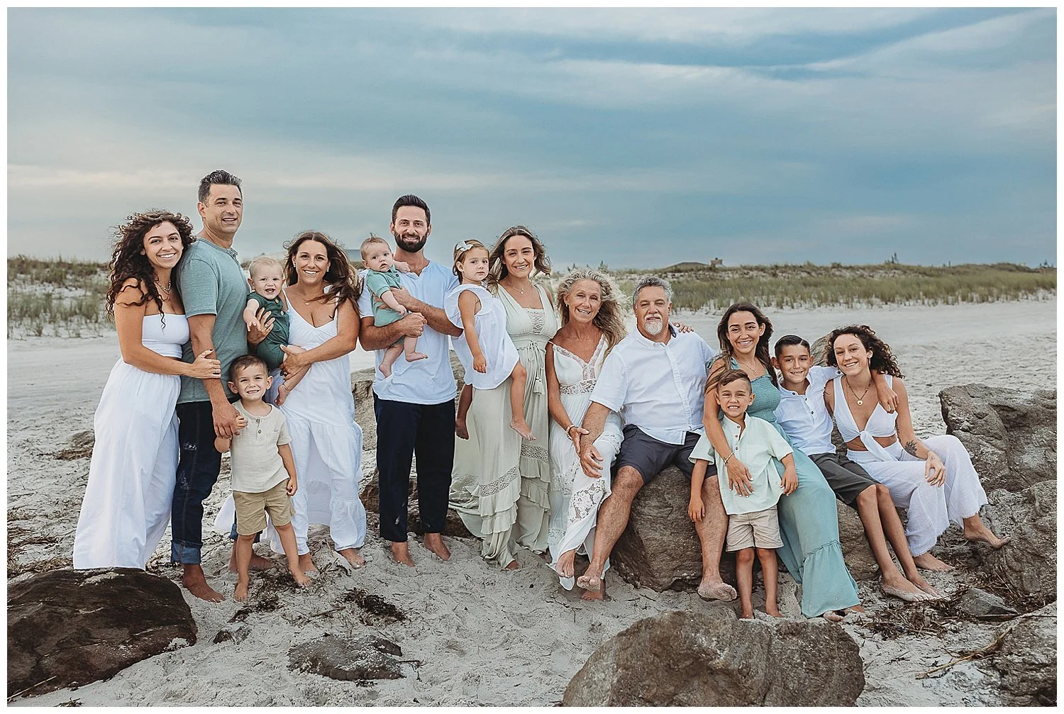 family dressed in white and green on the beach seated on a jetty