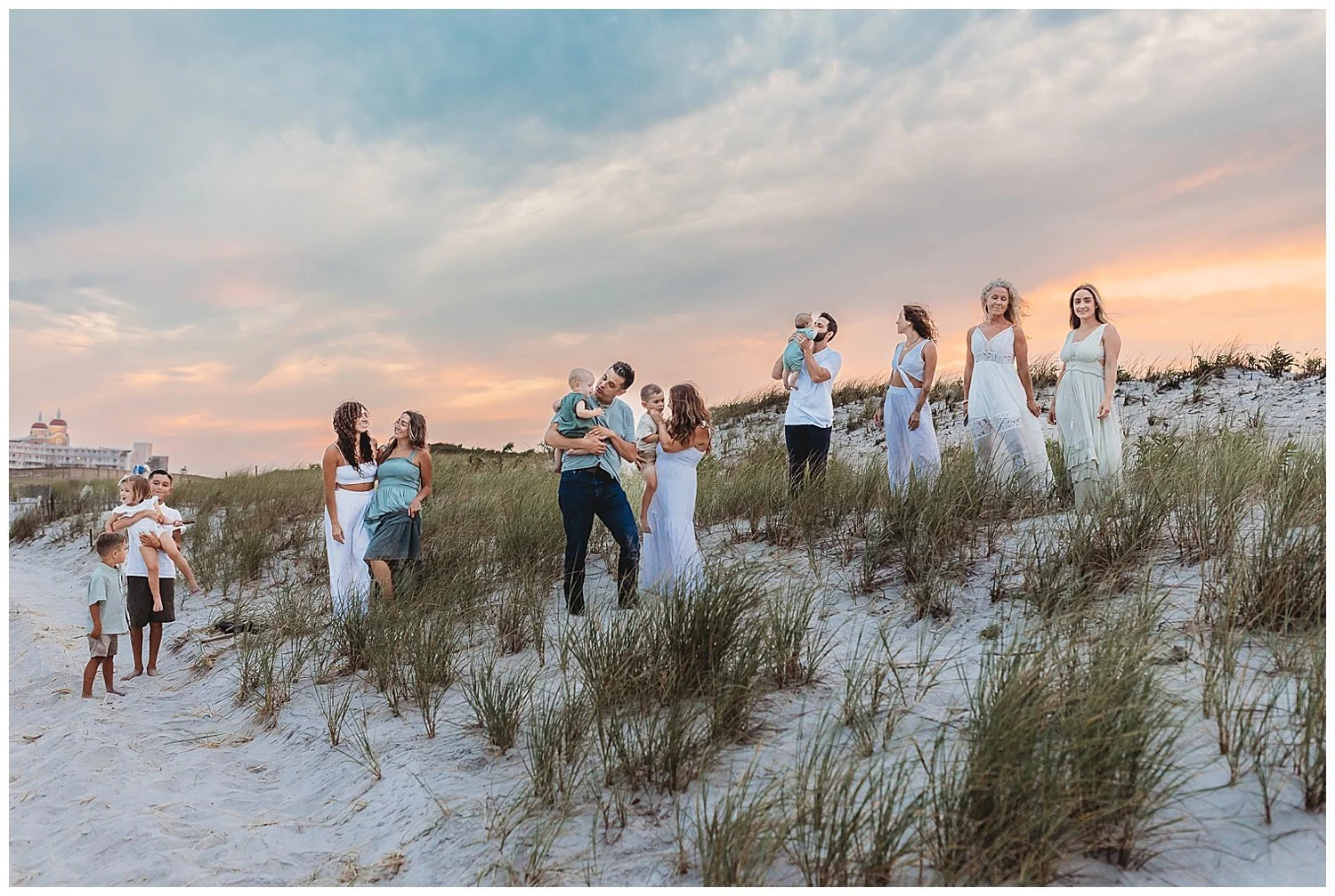 family standing on a jetty at the beach with pink and blue sunset sky behind them