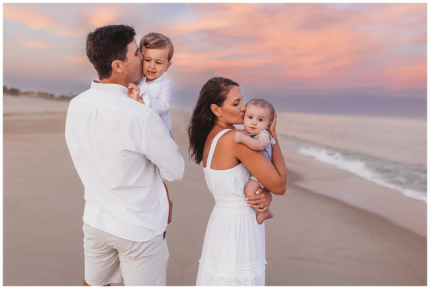 family embraced at sunset with a pink and orange sky kissing their children