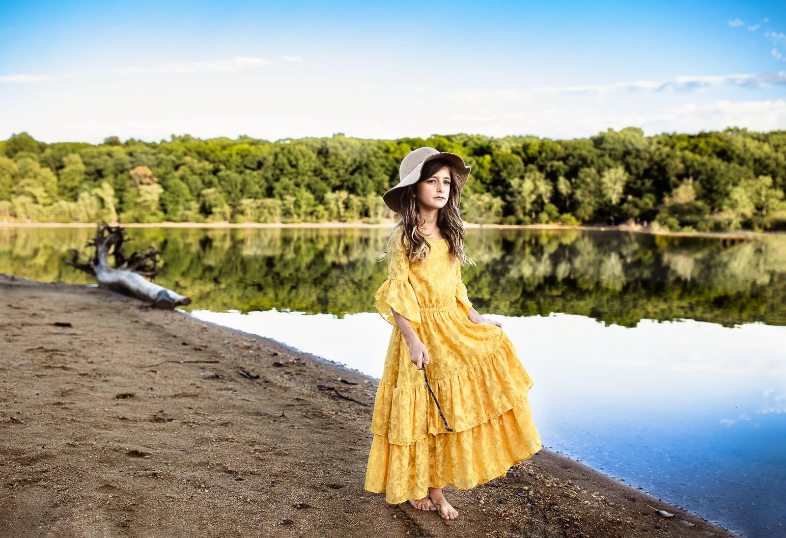 gilr in mustard yello boho maix dress and floppy hat on a beach with greens and a blue sky looking out at the water