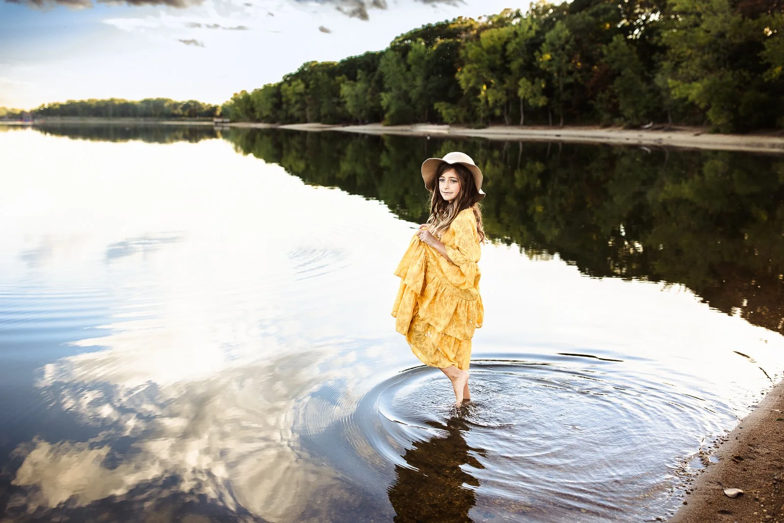 little girl in a lake looking out at water with a blue sky