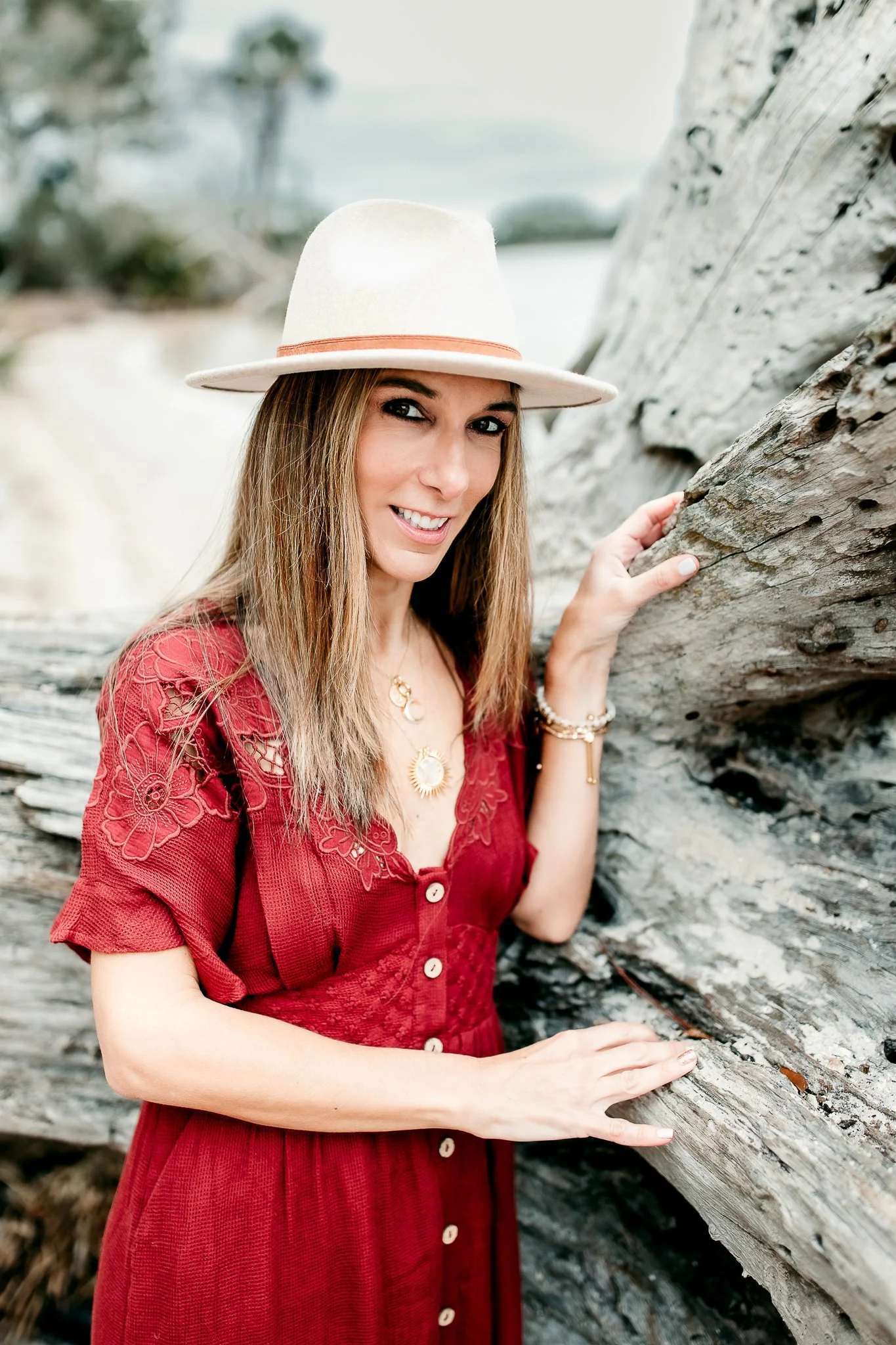 Teresa Geraghty a family and newborn photographer leaning against driftwood in a free people dress and boho hat for a headshot portrait on the intrcoastal