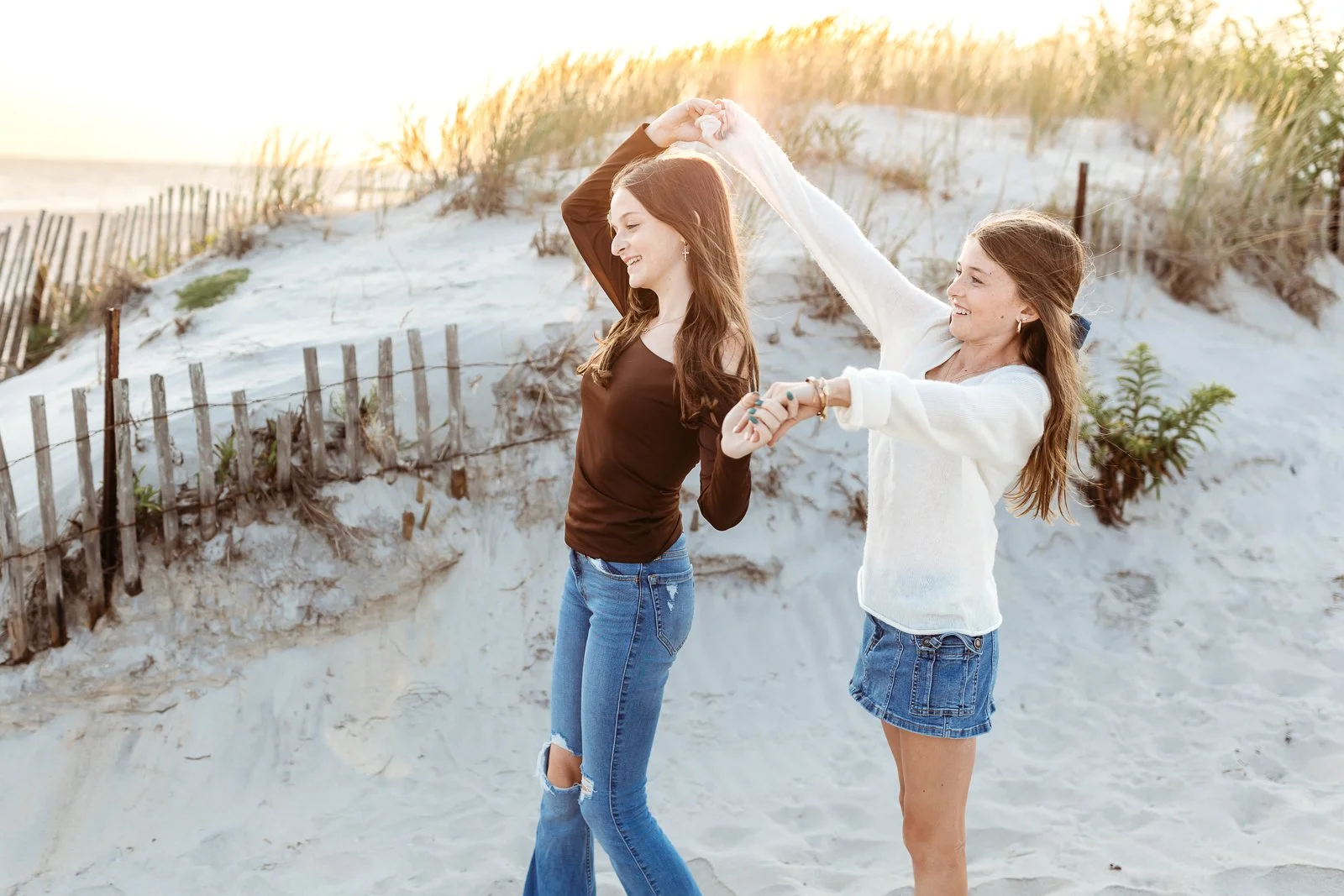 sisters dancing on the beach at sunset for family photos and they are laughing