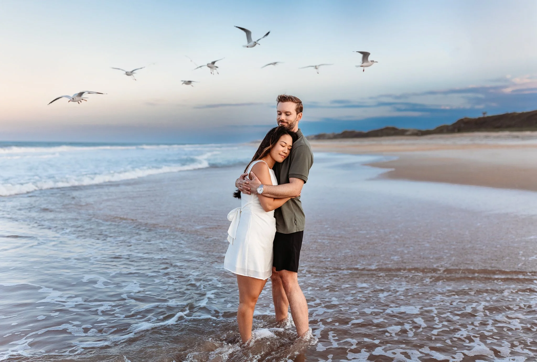 couple embraced on the beach with seagulls flying around them