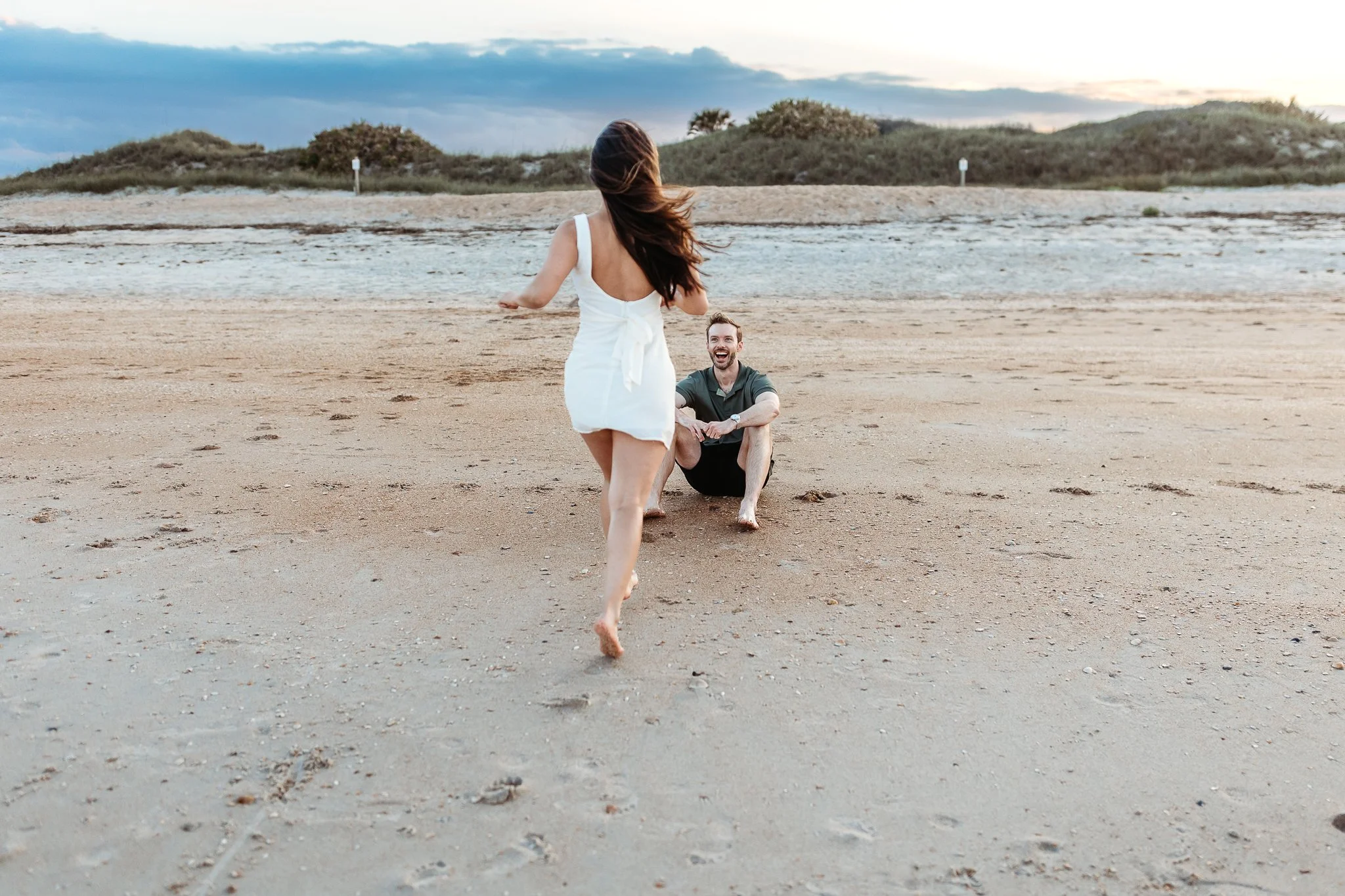 woman running on the sand to her fiancé and he is laughing
