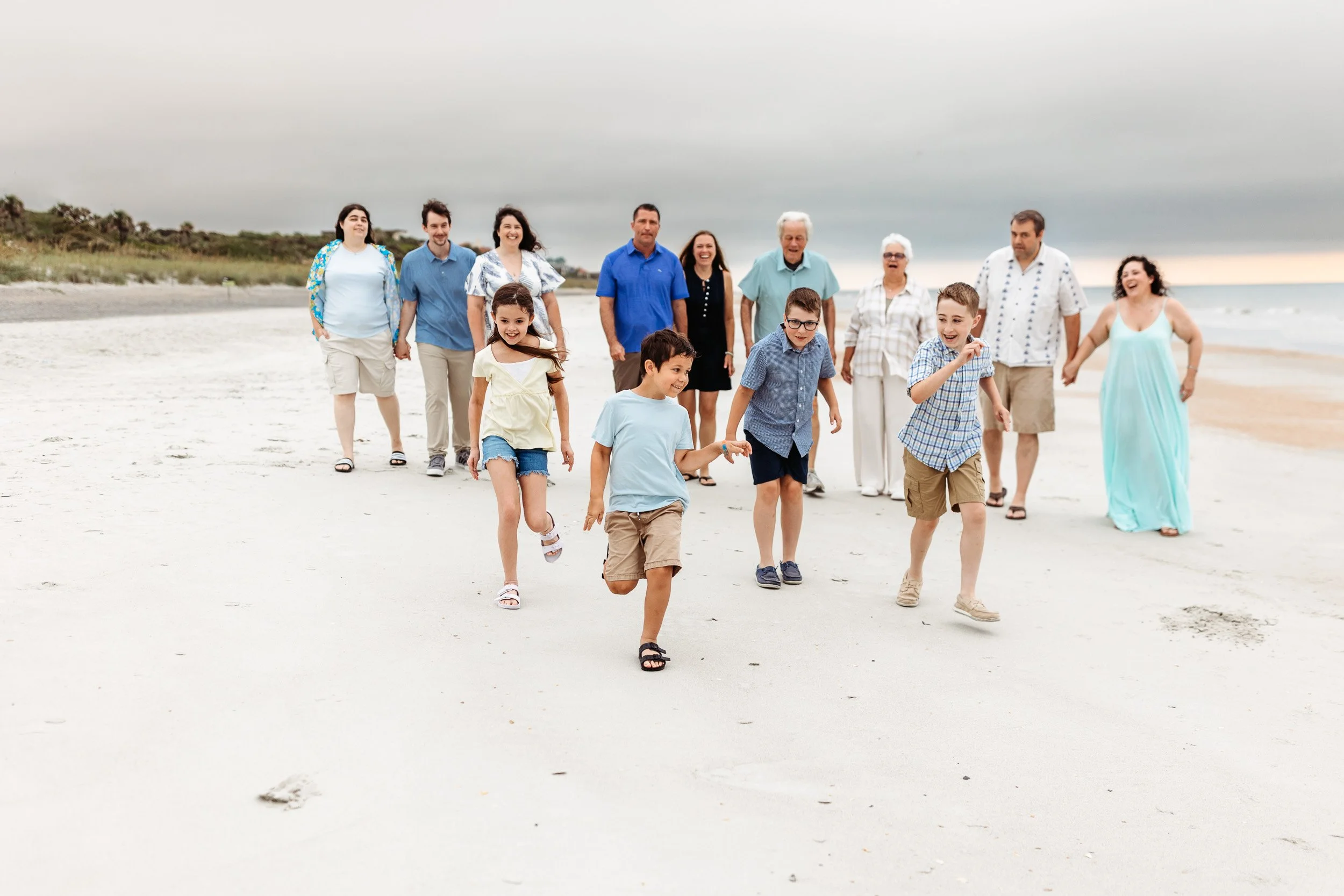 extended family walking along the beach at sunrise and the grandchildren are running ahead and they are all laughing