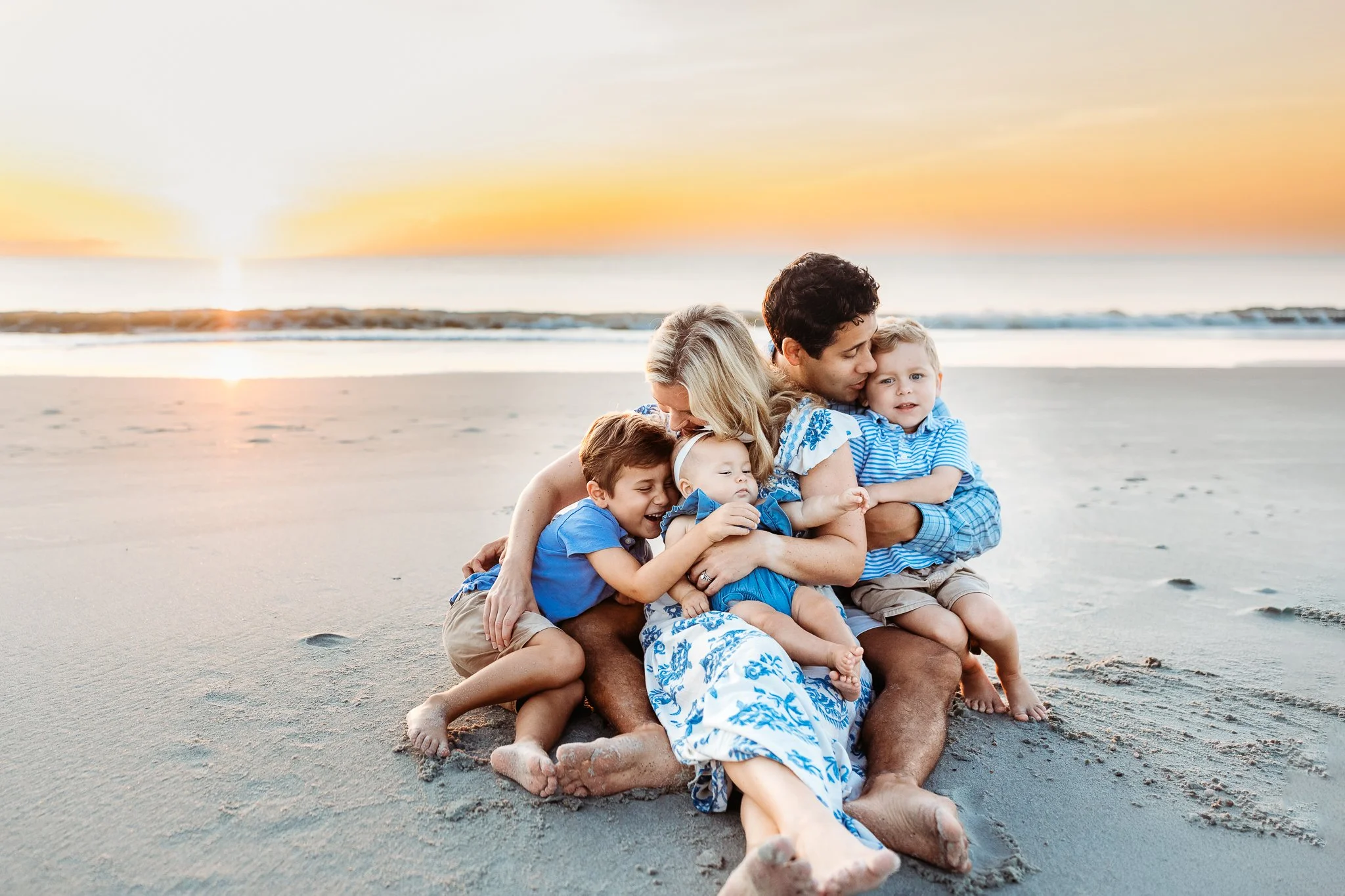family embraced and cuddled up on th beach at sunrise kissing each other