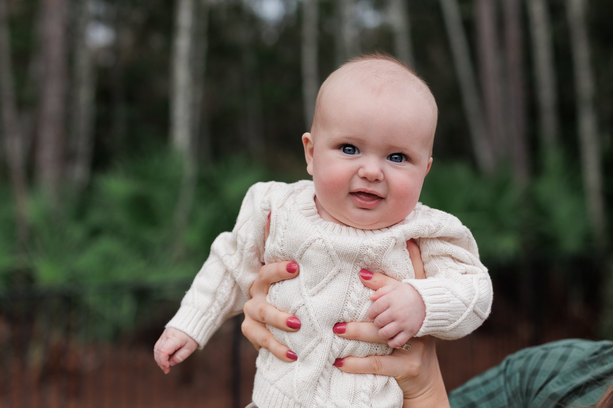 baby in a white seater being held in the air and he is laughing