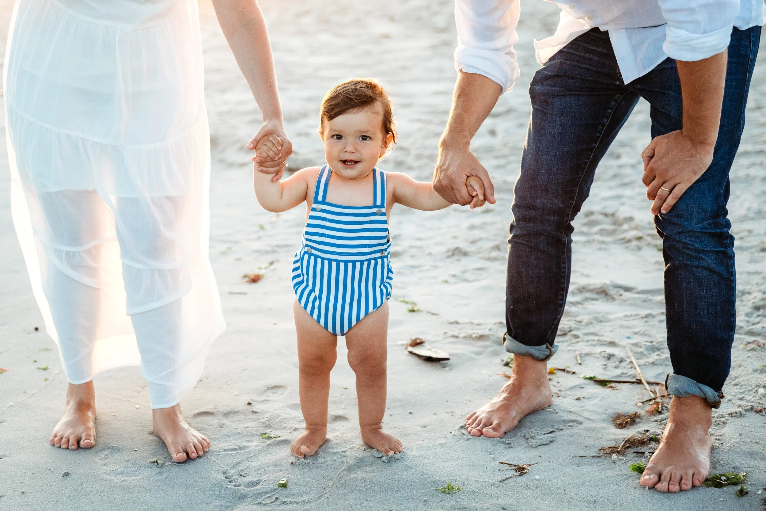 Baby holding parents' hands on the beach during a St. Augustine first birthday photo session