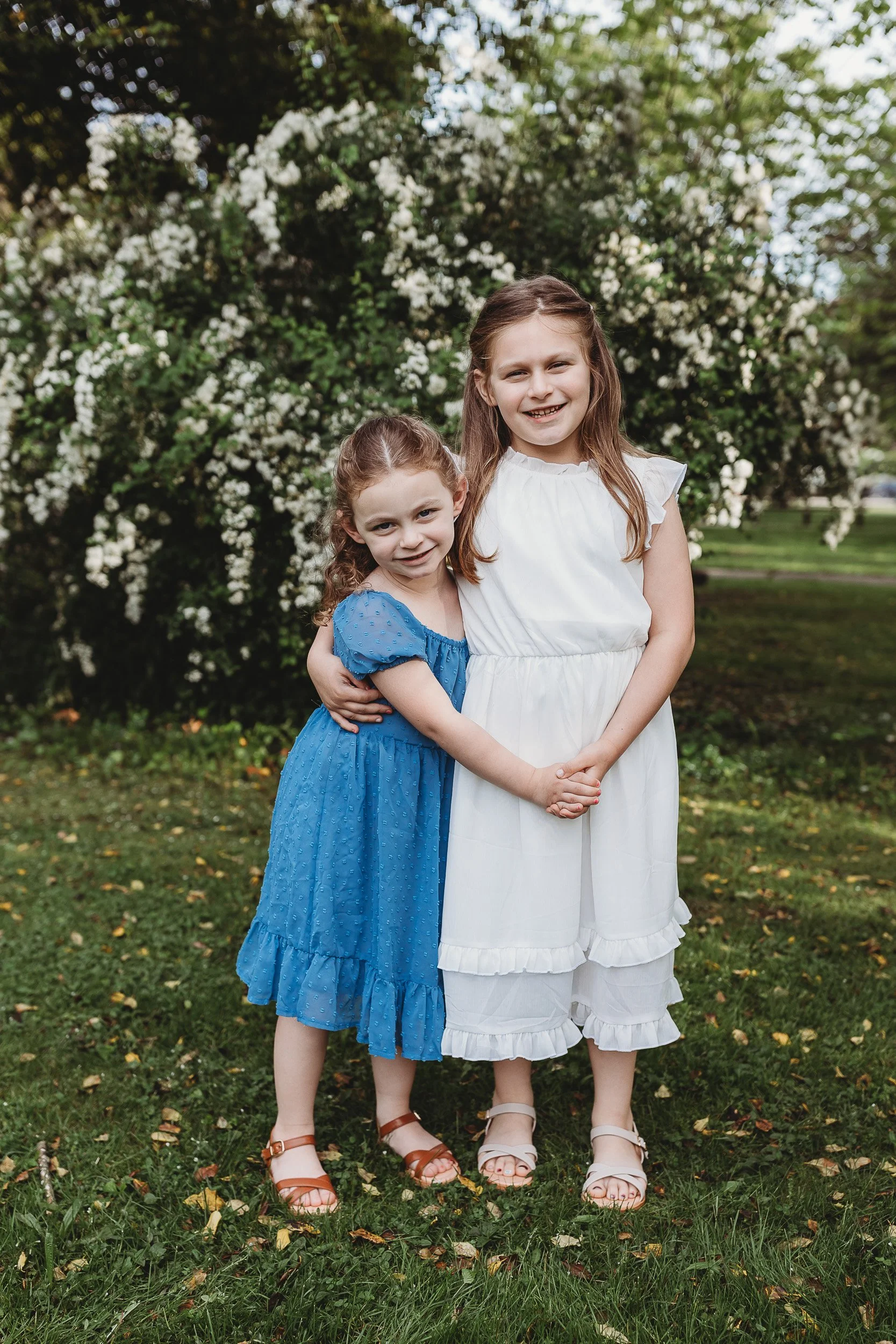 girls in easter dresses in front of white flowers embraced for their Jacksonville family photos