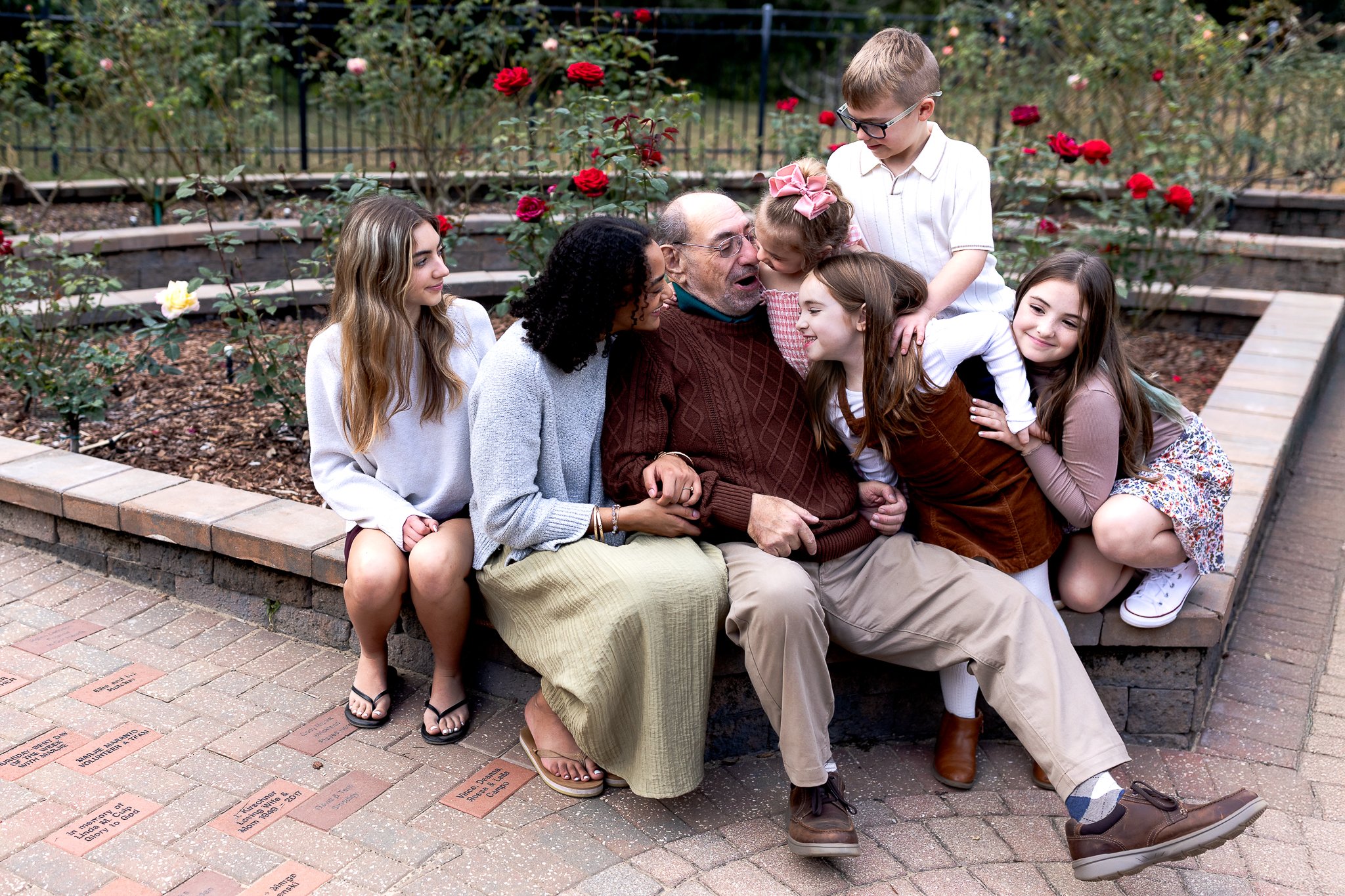 grandpa seated with grandchildren In a rose garden and they are jumping on him and laughing