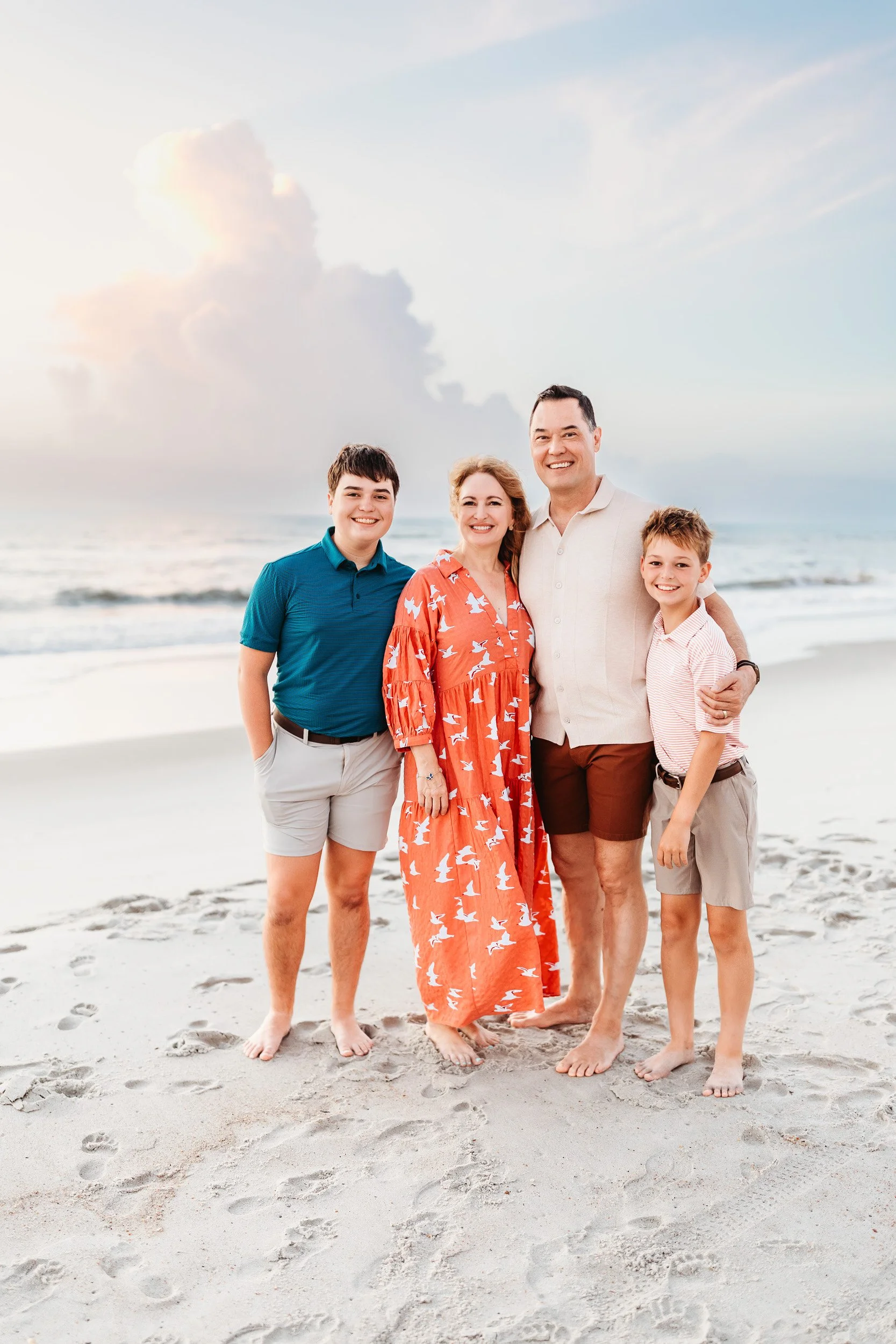 family pn the beach at sunrise with a beautiful and fluffy pink cloud behind them