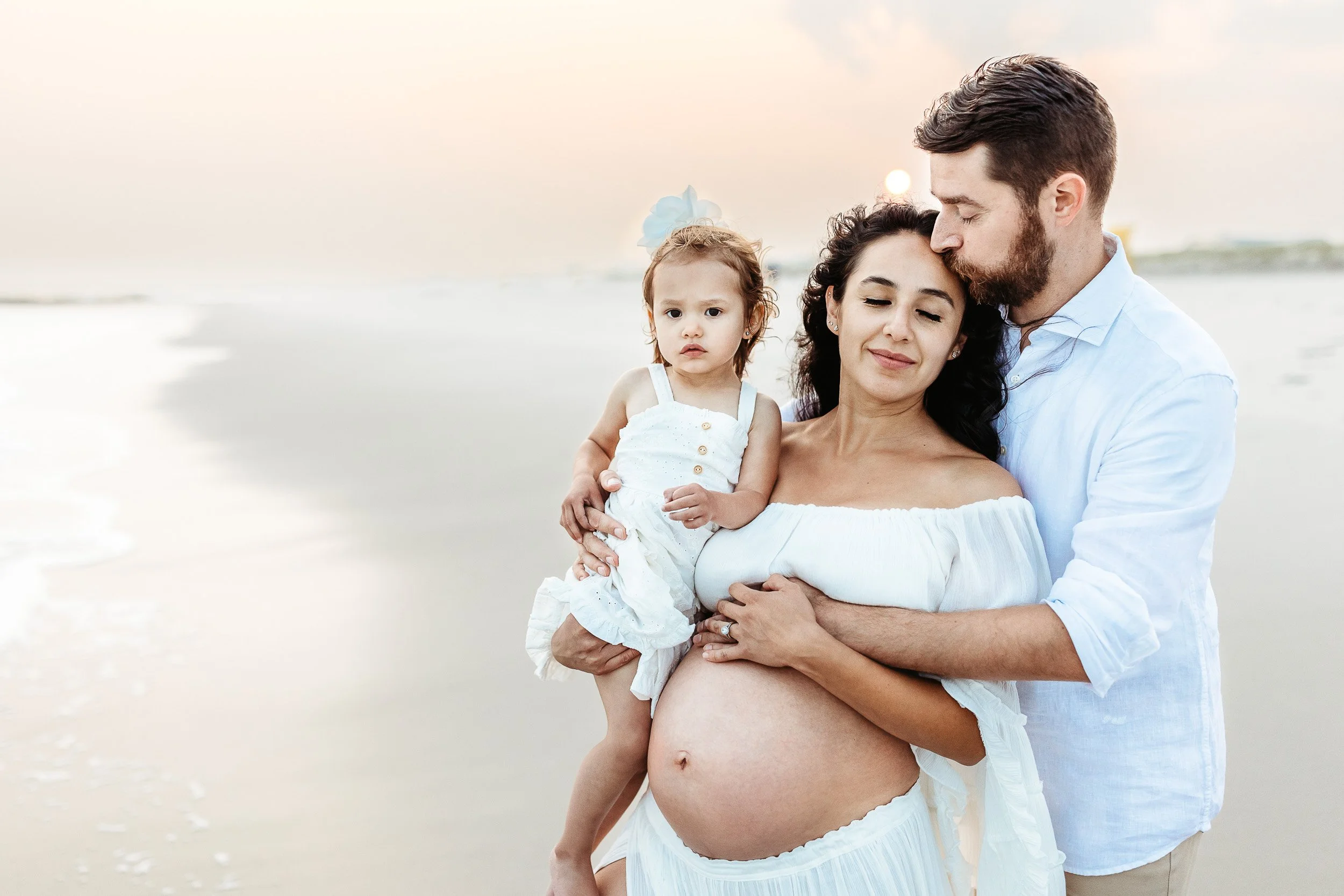 pregnant woman leaning into man who kisses her on forehead at Atlantic beach maternity photo session