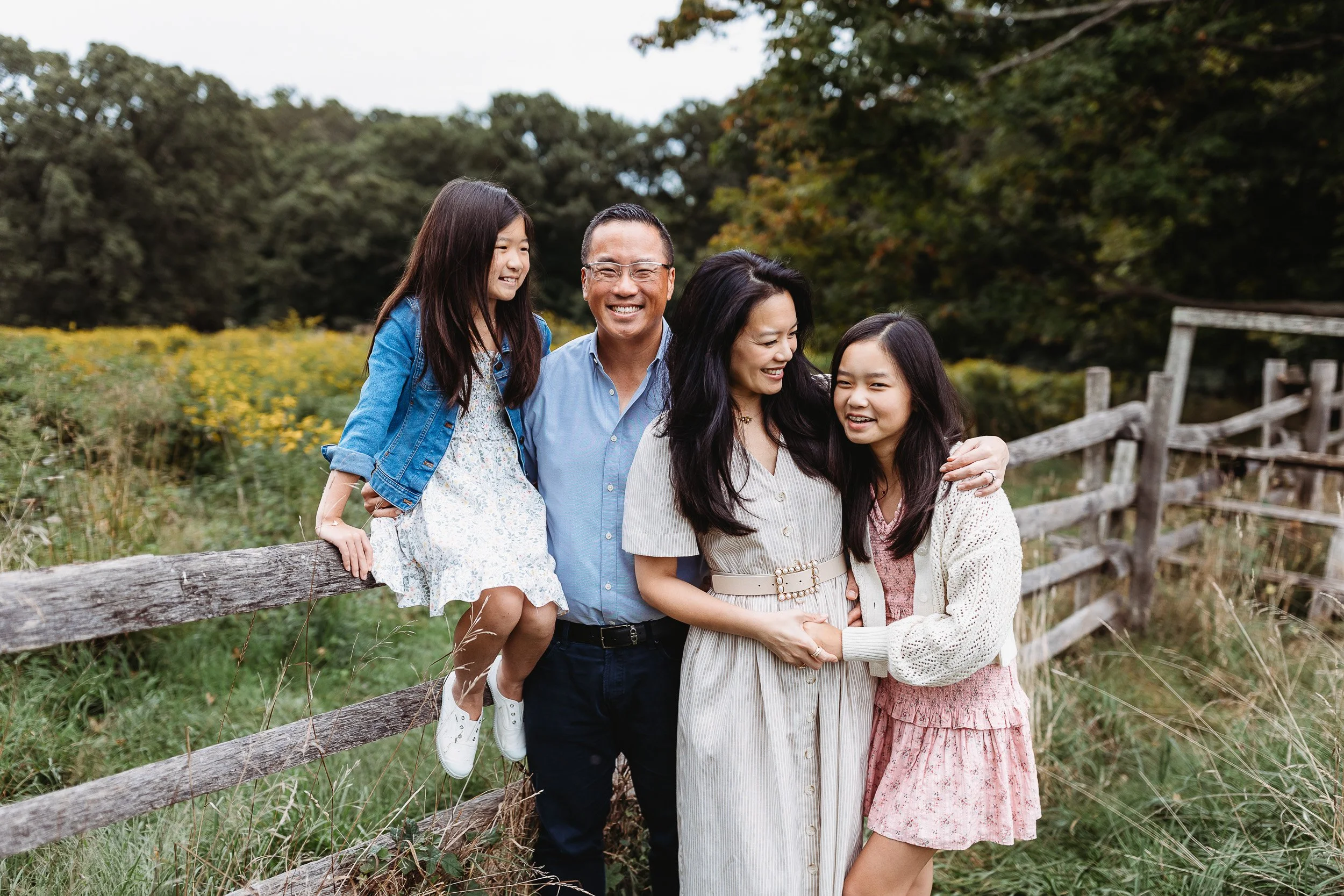 family on a wooden fence at a farm in Jacksonville for family photos and they are laughing