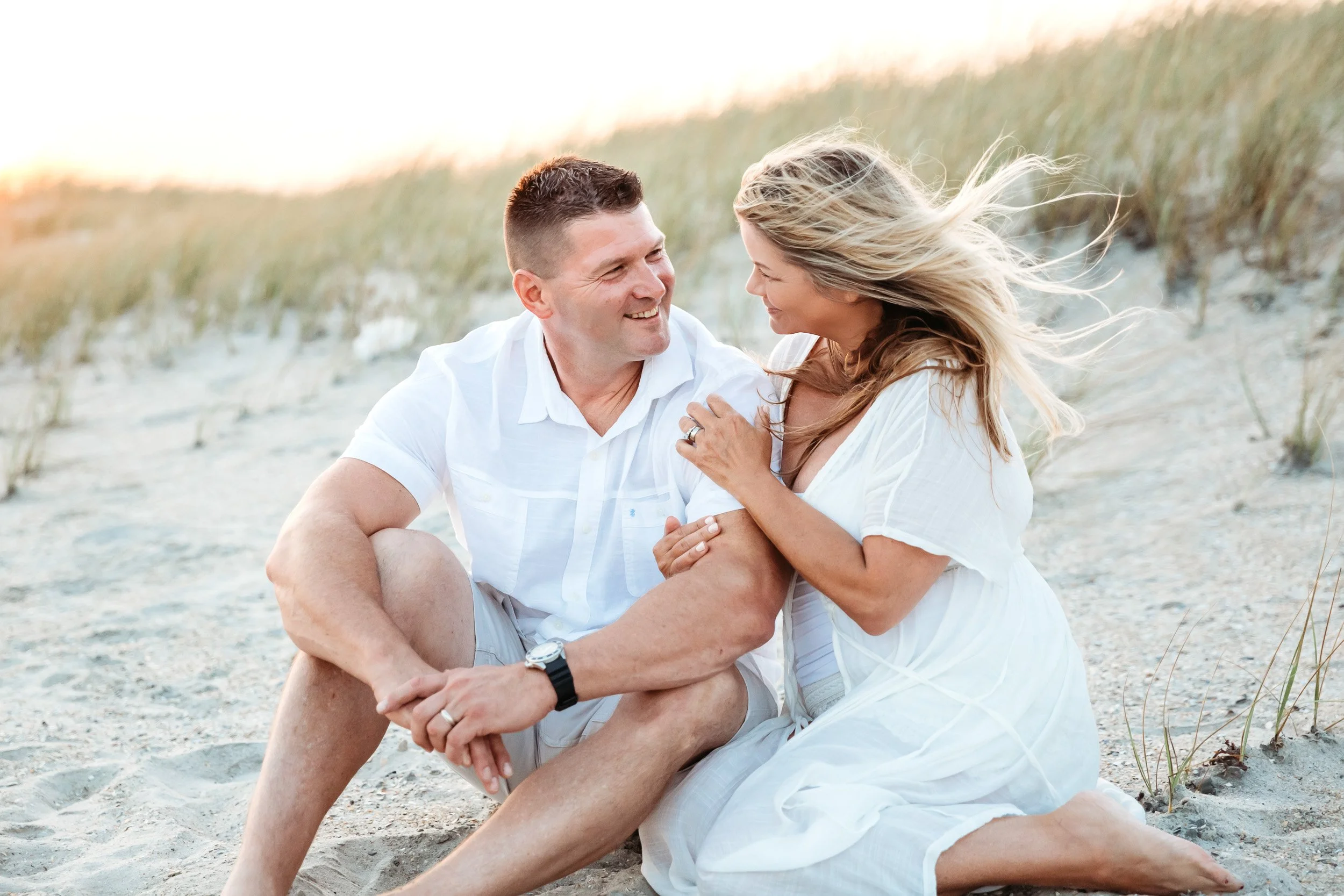 husband and wife seated on the dune at guana middle beach and laughing at sunset while kids play on the beach