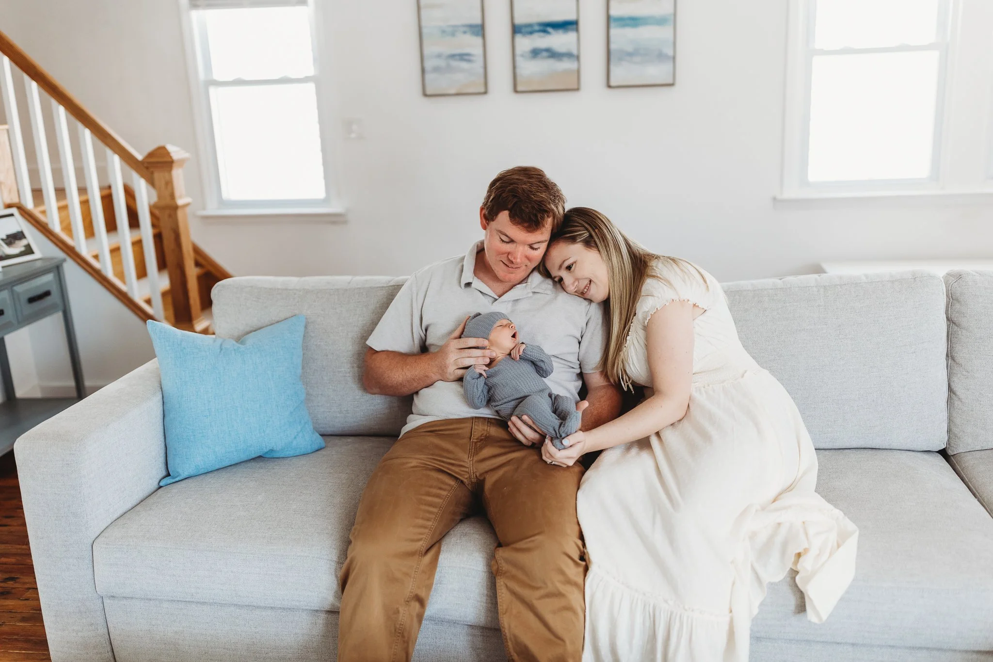 mother and father sitting on a couch holding a swaddled newborn baby