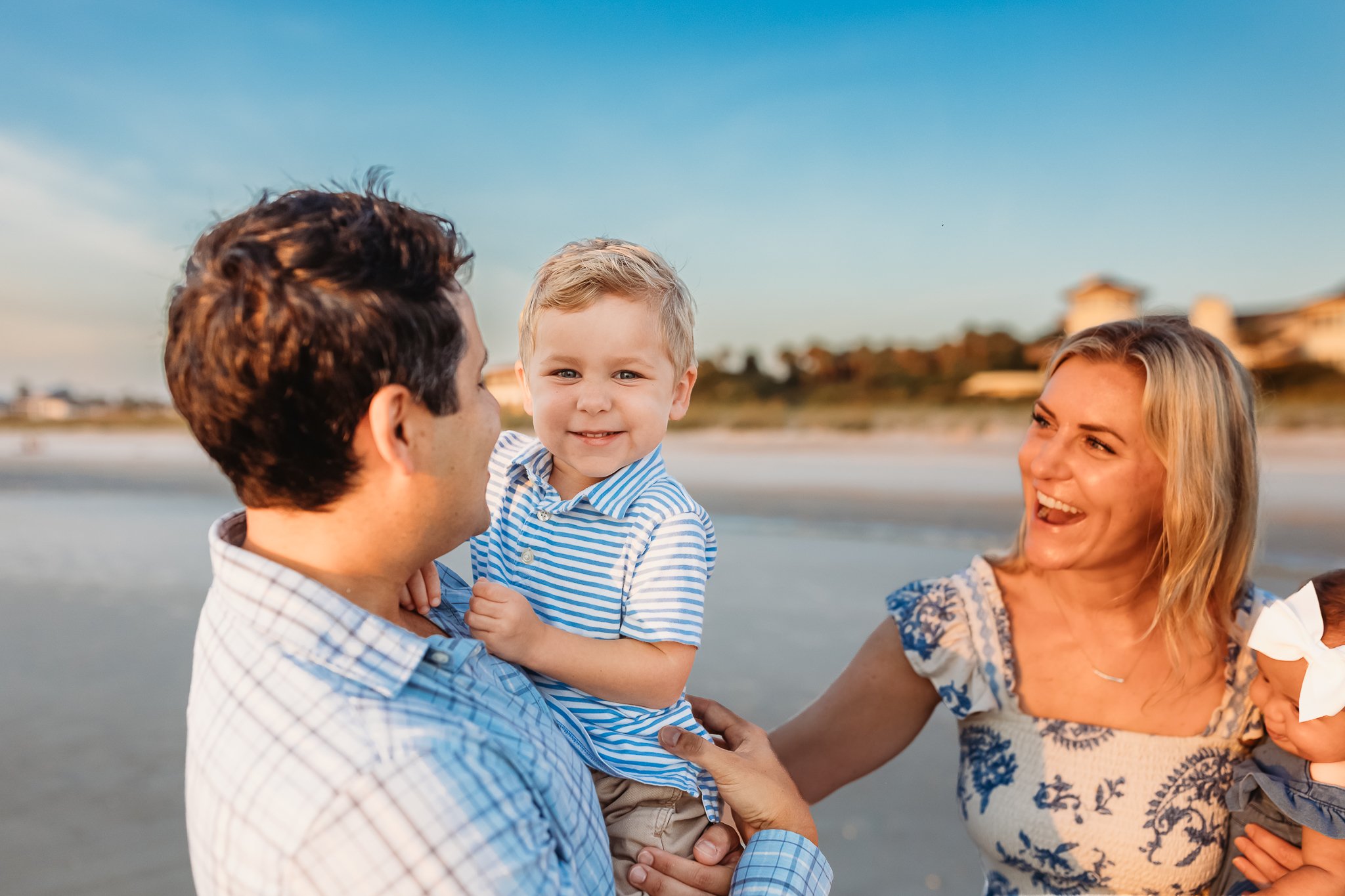 dad holding toddler who is laughing and looking at the camera and mom is watching