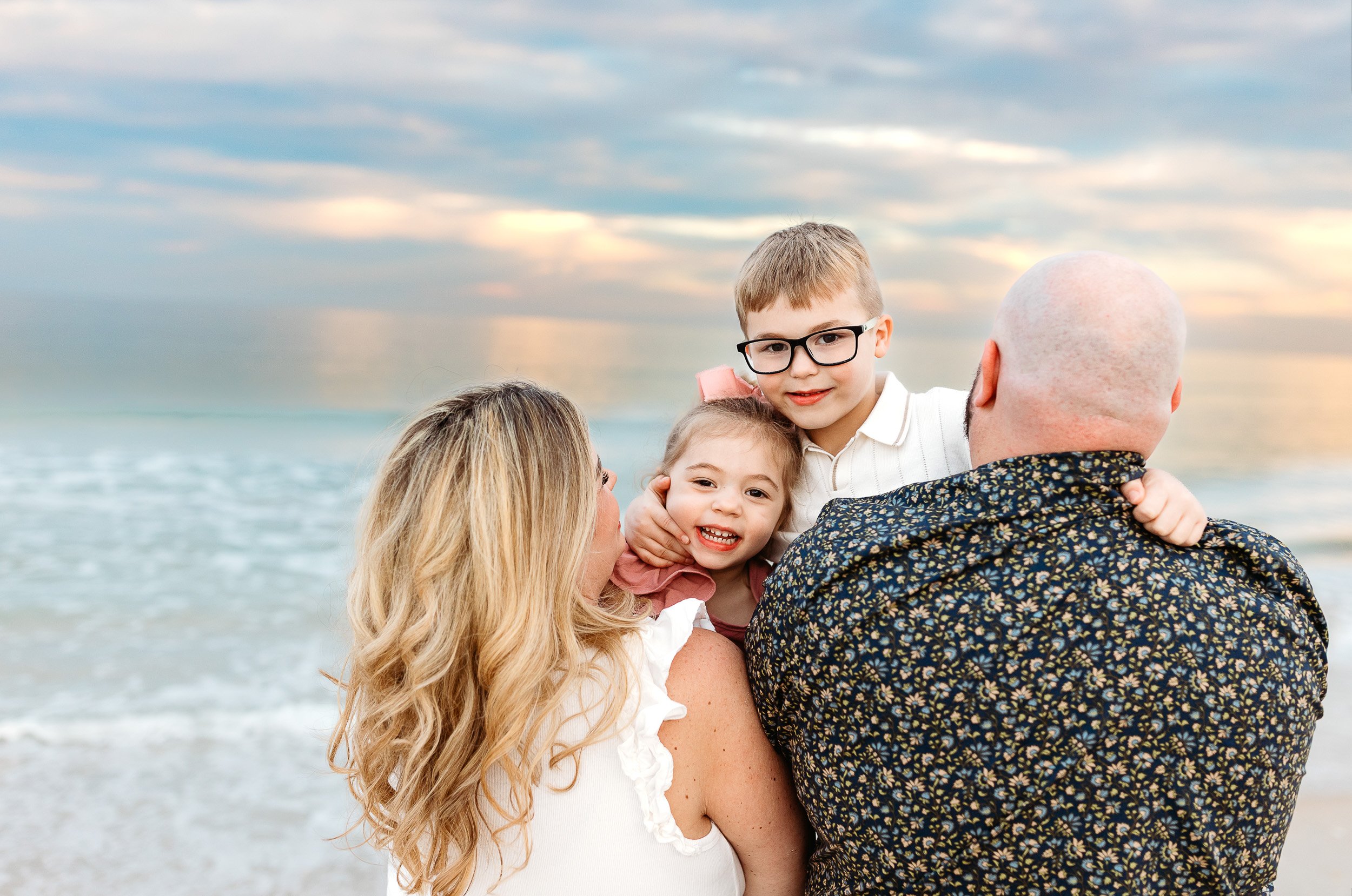 kids playing peek a boo over the shoulder of parents at sunset at the beach