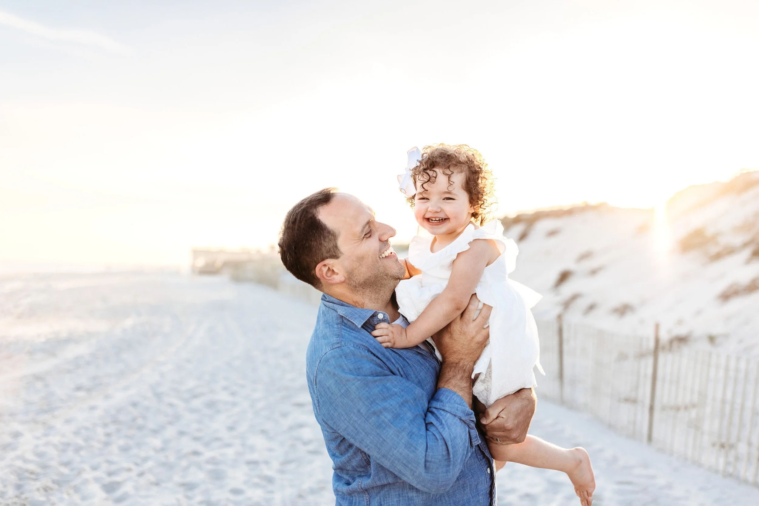 dad lifting his toddler daughter in the air and they are both laughing and they are on the beach at crescent beach at sunset