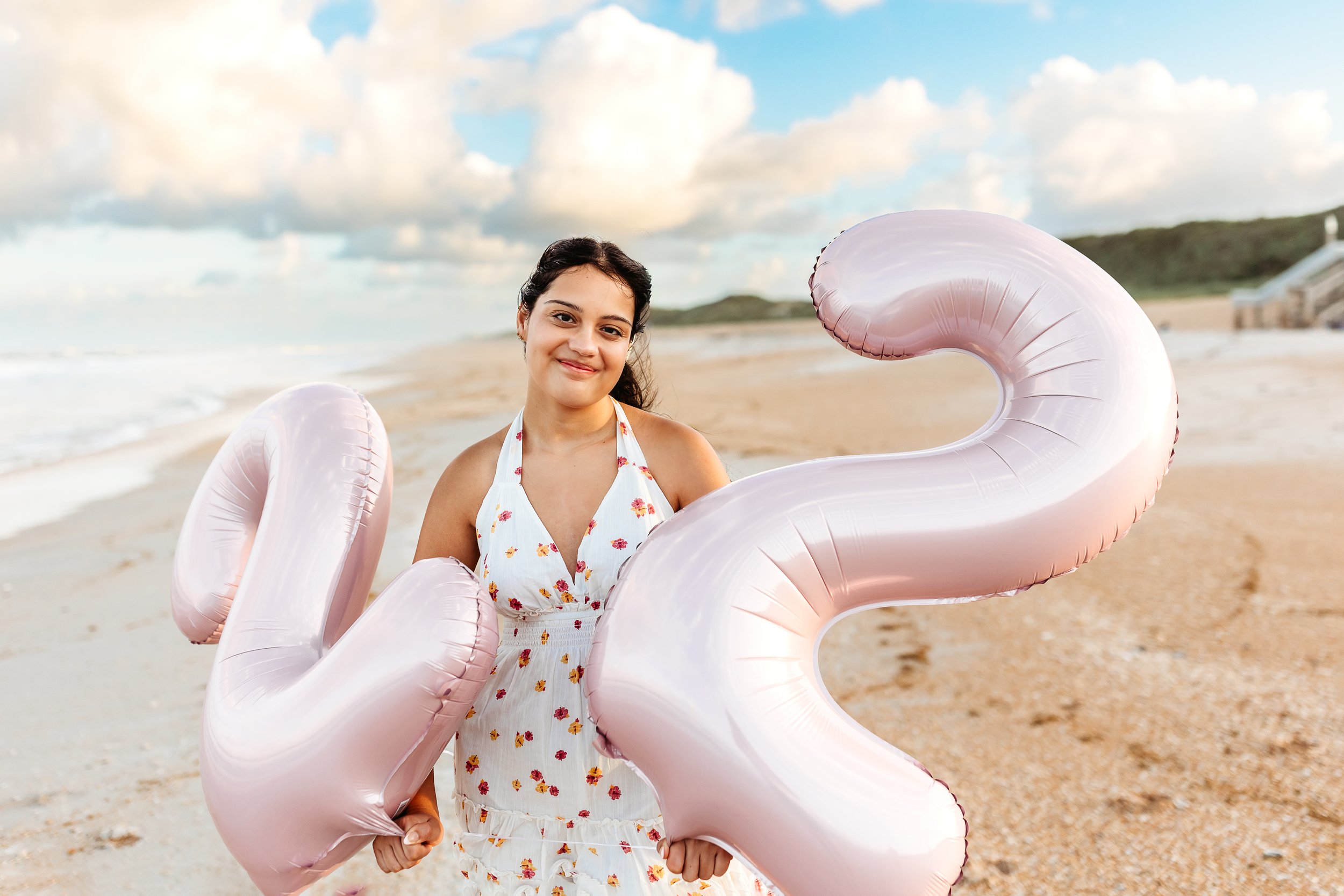 close up of girl with pink 22 balloons on the ocean's edge smiling