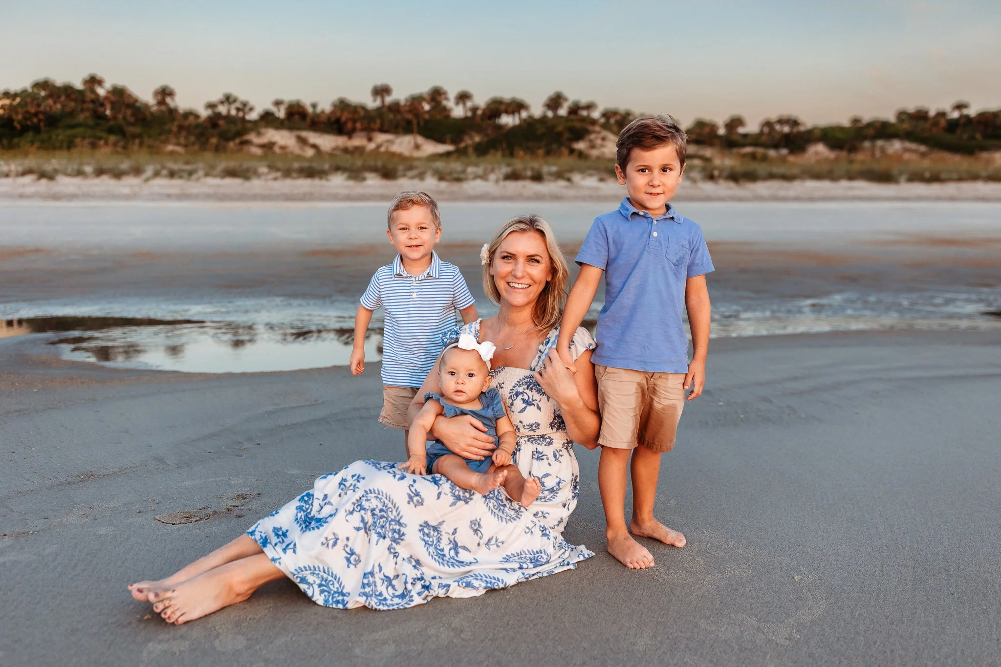 mother seated on the sand with her children and a dune is behind her they are all looking at the camera