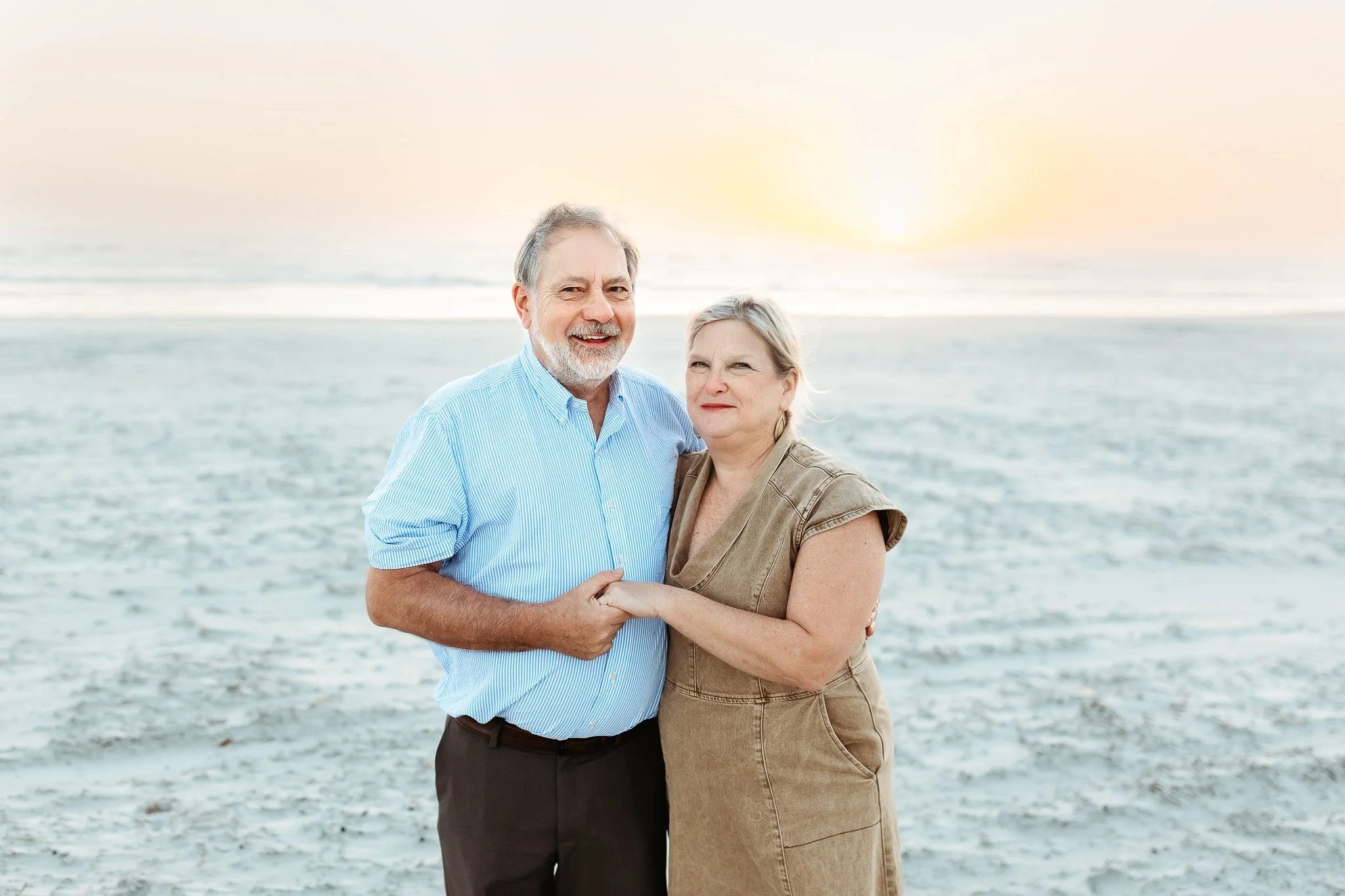 Grandparents smiling together at sunrise on Crescent Beach during a milestone family photo session.