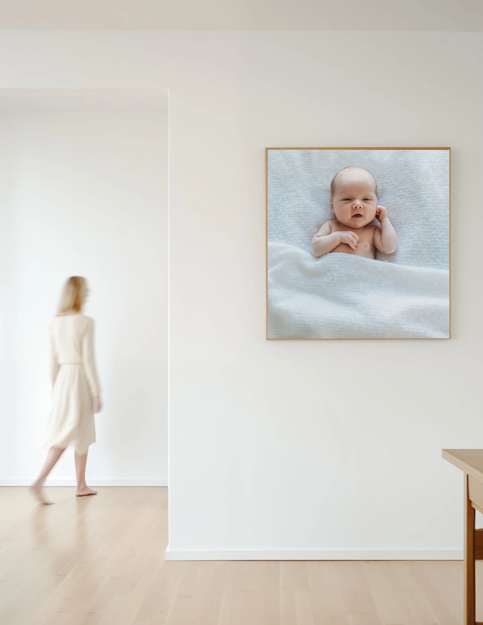 woman walking in a Hall and their is an image from a Jacksonville newborn photo session of a baby sleeping on a white bed on the wall 