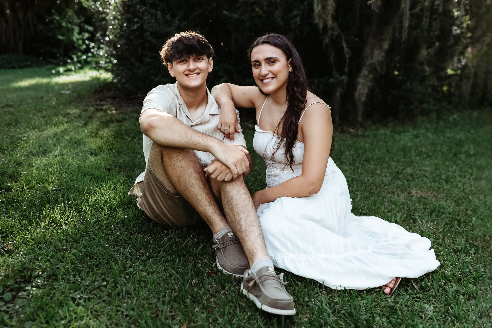 adult siblings seated on the gras sin front of moss for a portrait before one leaves for college