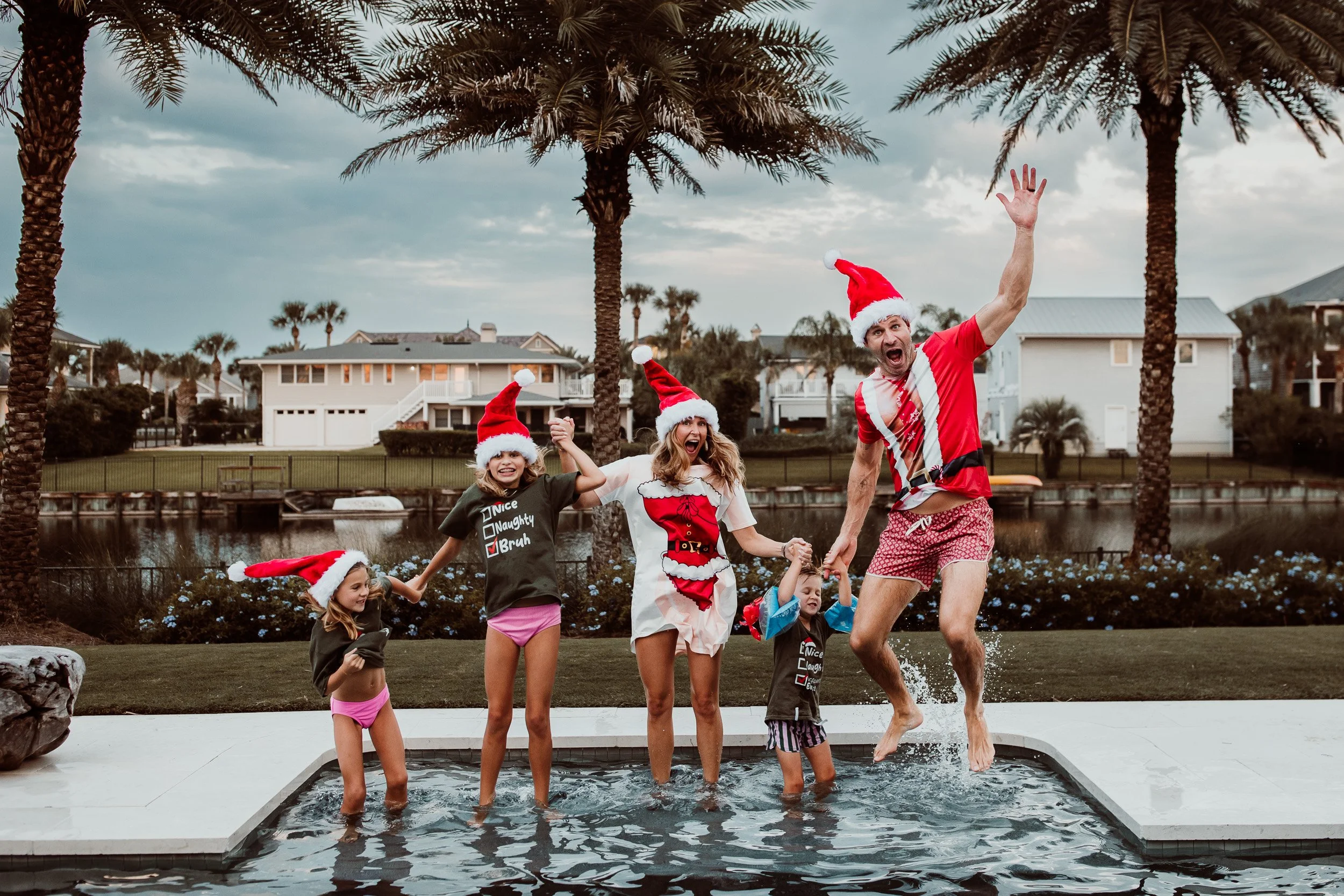 family in Santa hats and christmas t shirts jumping into a pool and laughing