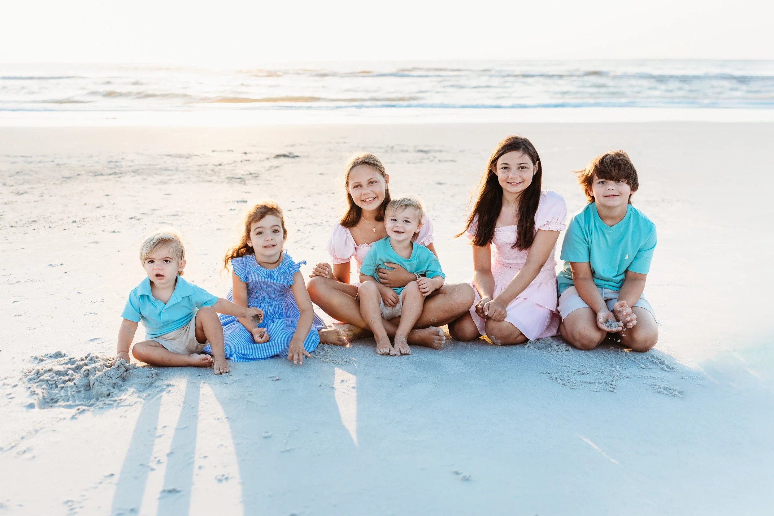 cousins seated on a beach laughing during family photos