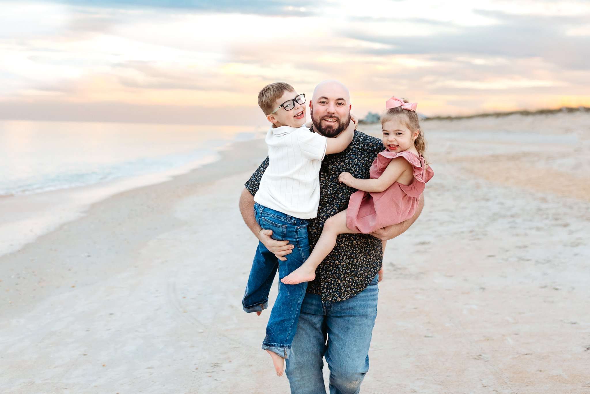 dad running with children who are laughing on the beach at sunset