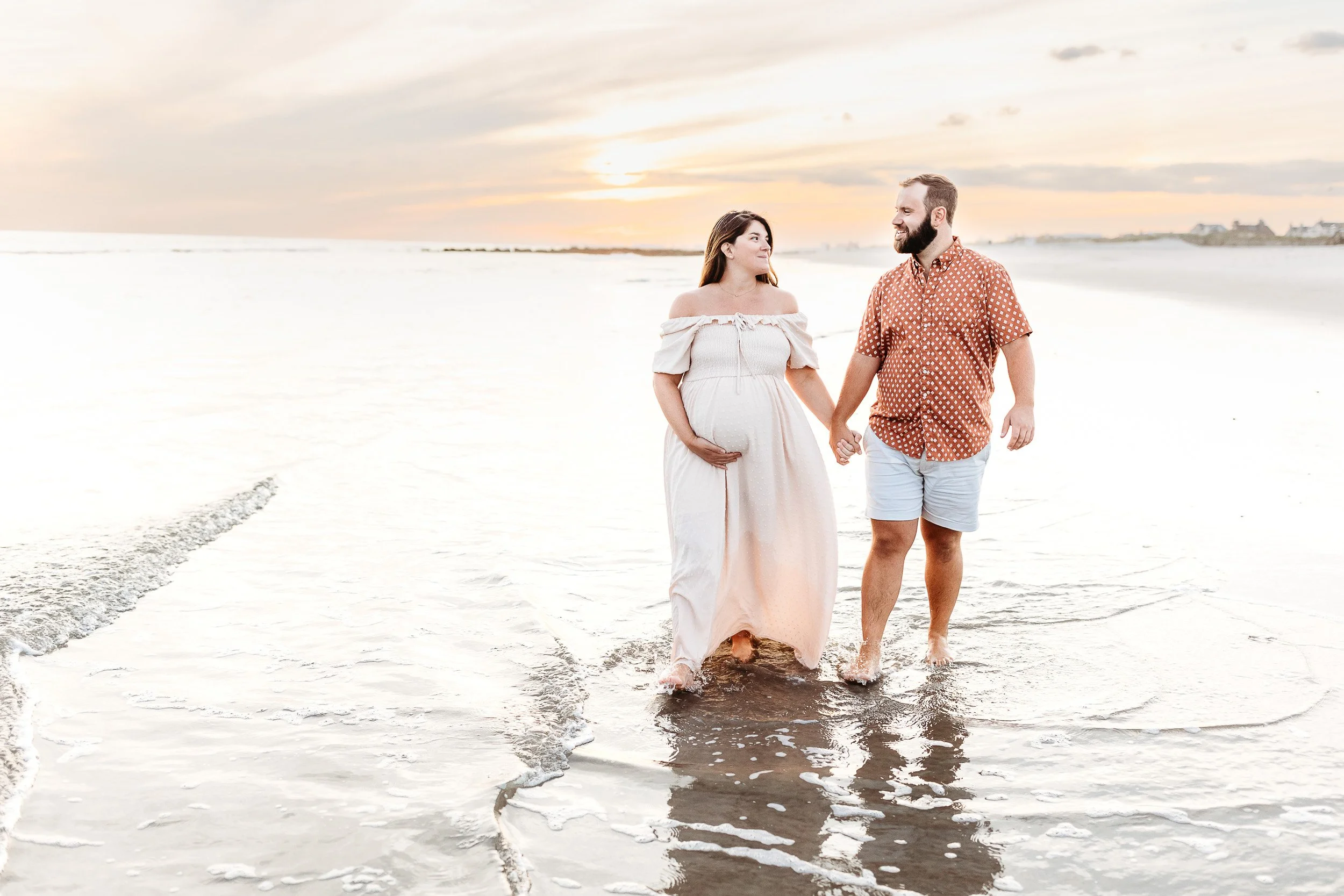 Couple expecting baby walking along St. Augustine beach during babymoon