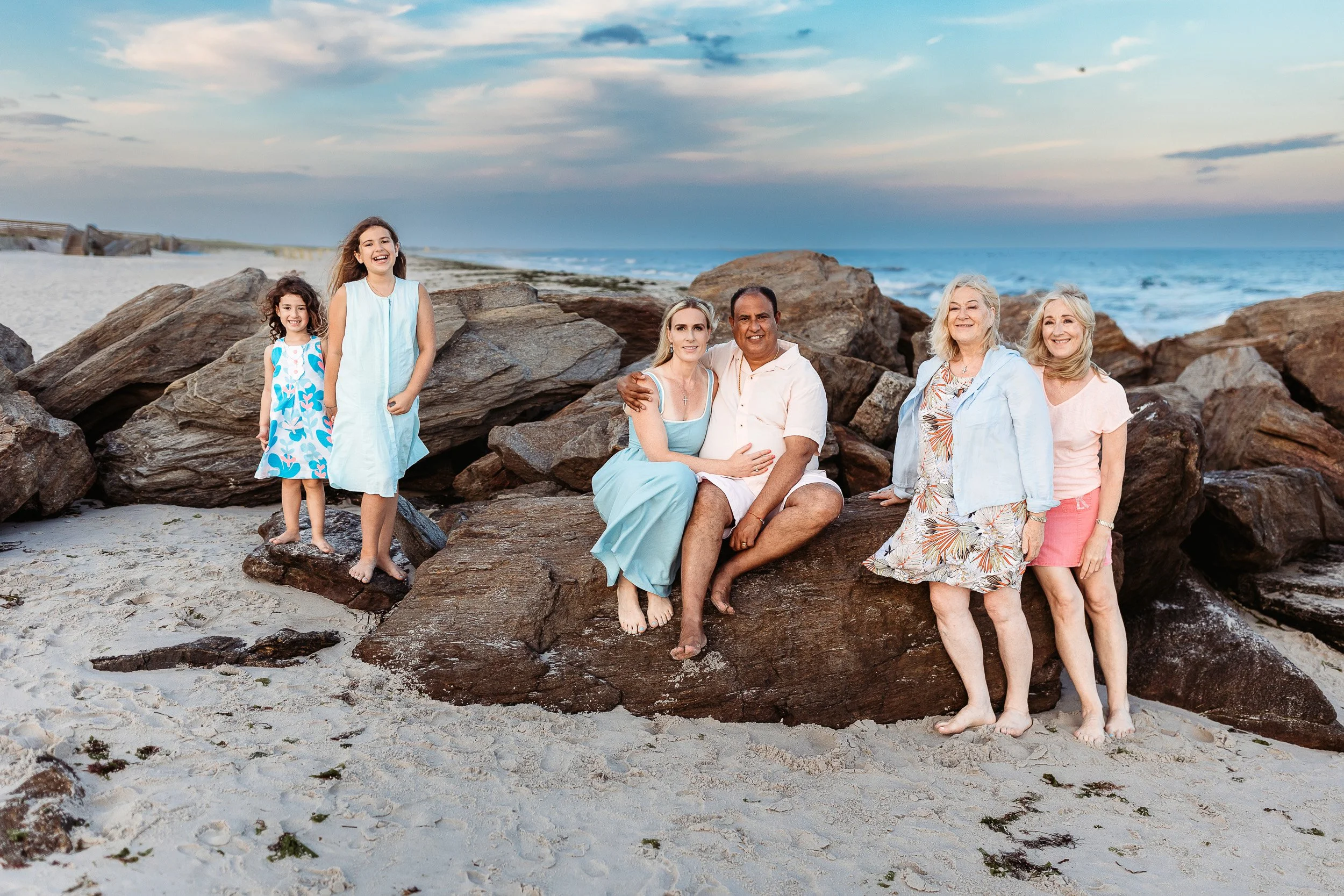family seated staggered on a jetty and the children are laughing.  family dressed in pinks and blue 