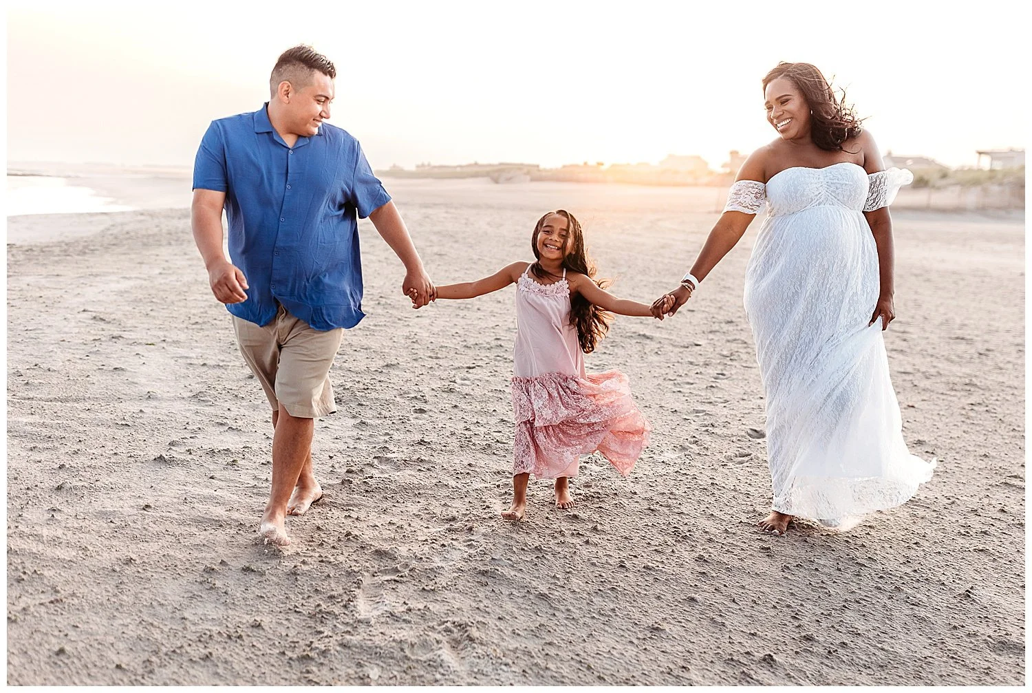 family holding hands walking on the beach laughing with sunset behind them