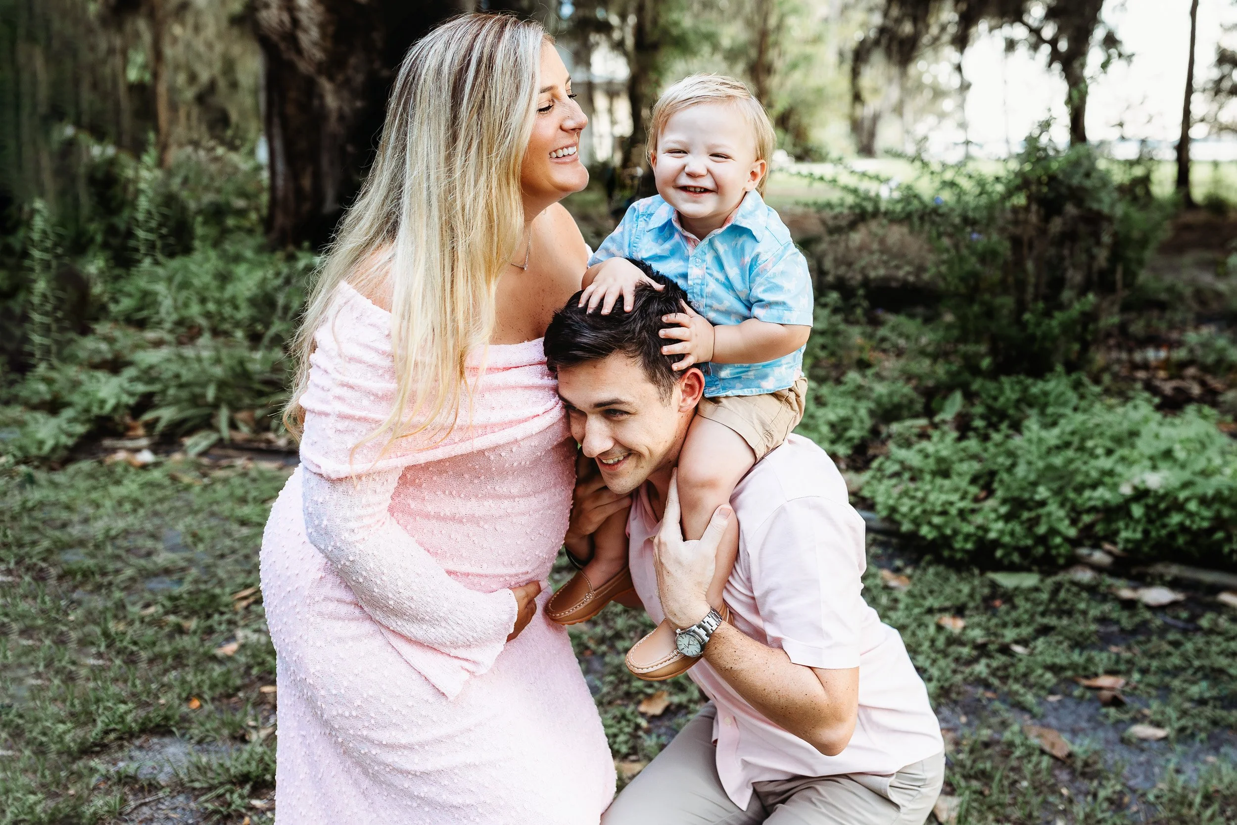 toddler on dad's shoulders and he is laughing while mom looks at him