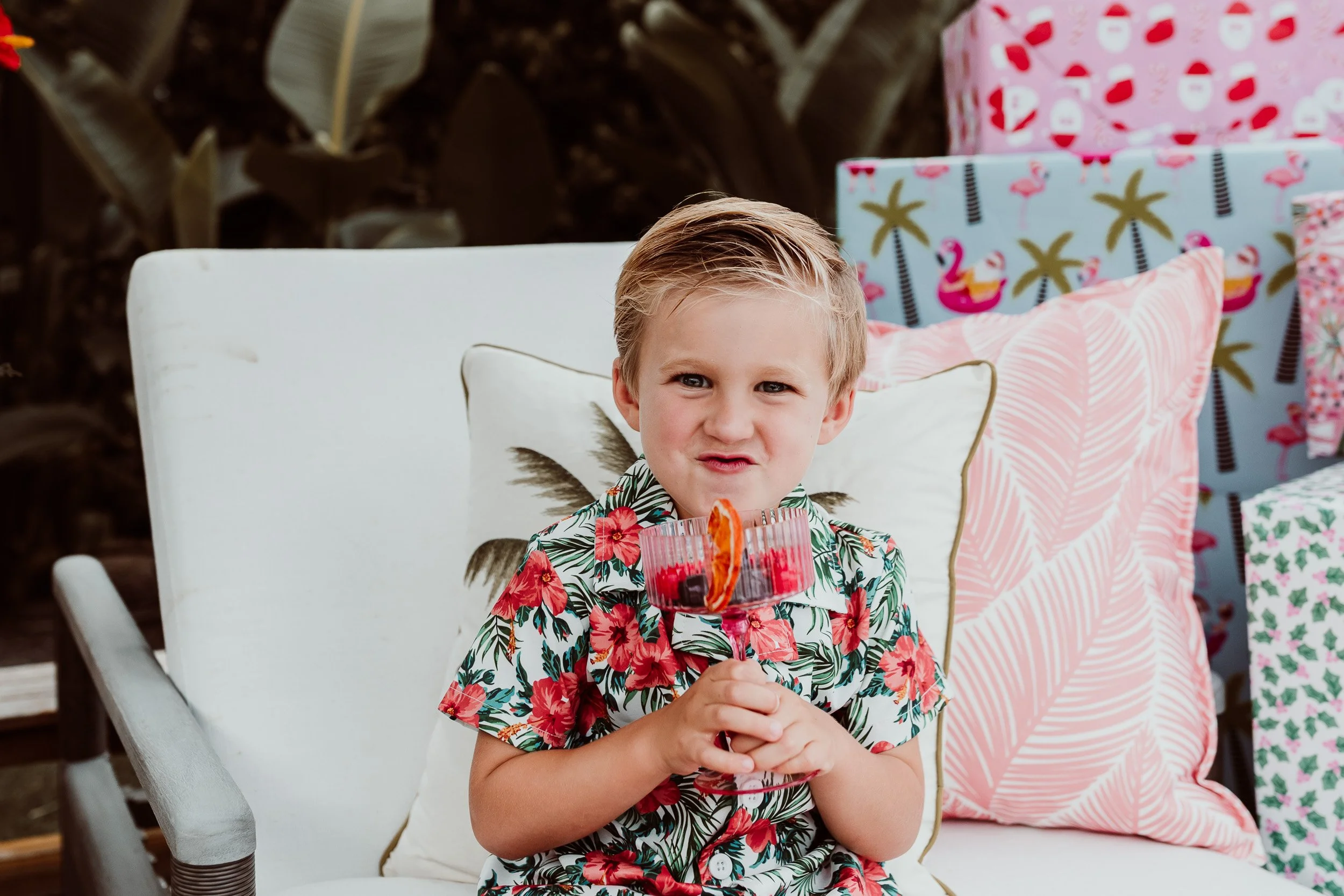 come up of little boy drinking a mocktail by the pool in a hawaain holiday shirt