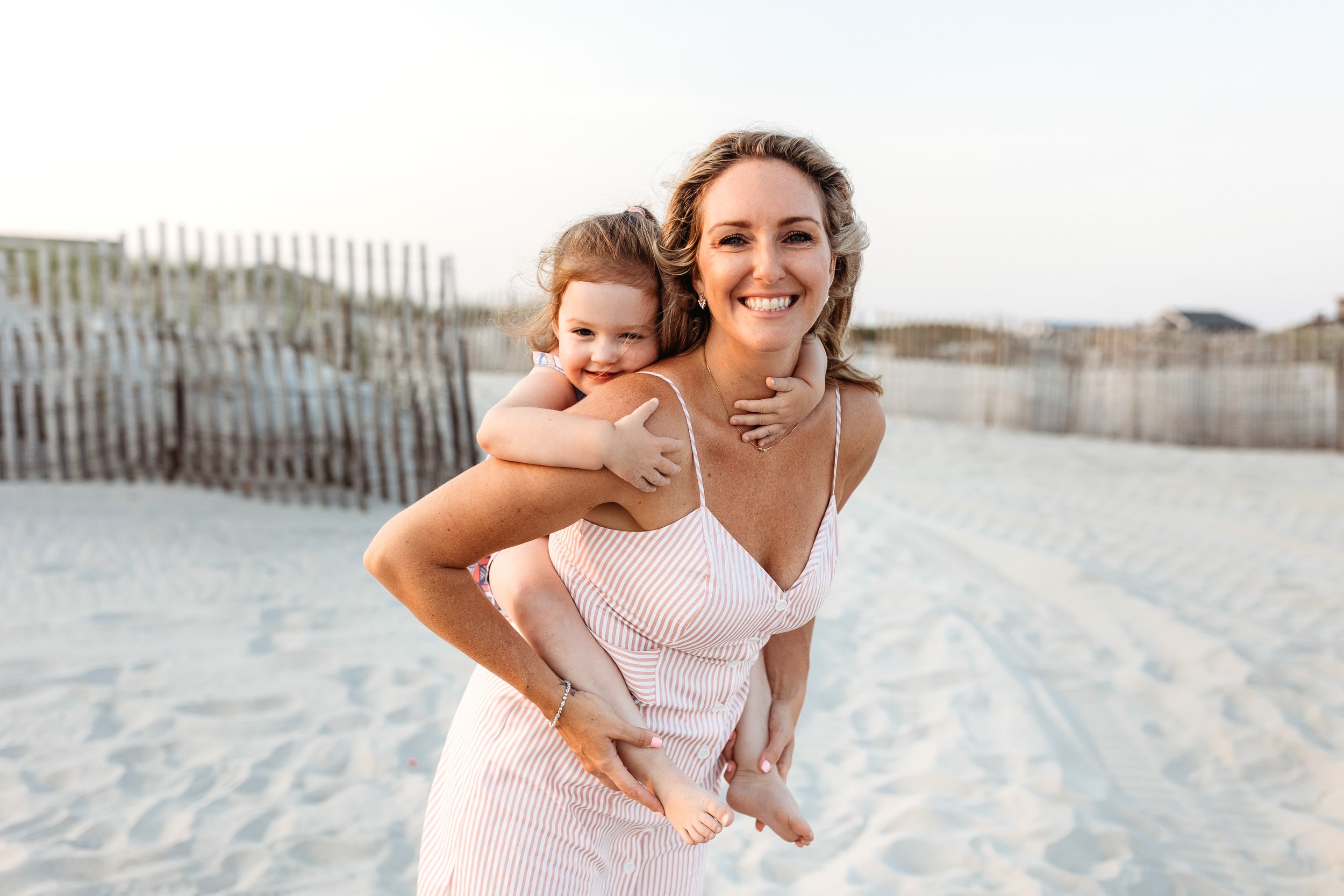 mother carrying toddler piggy back style on the beach and she is laughing
