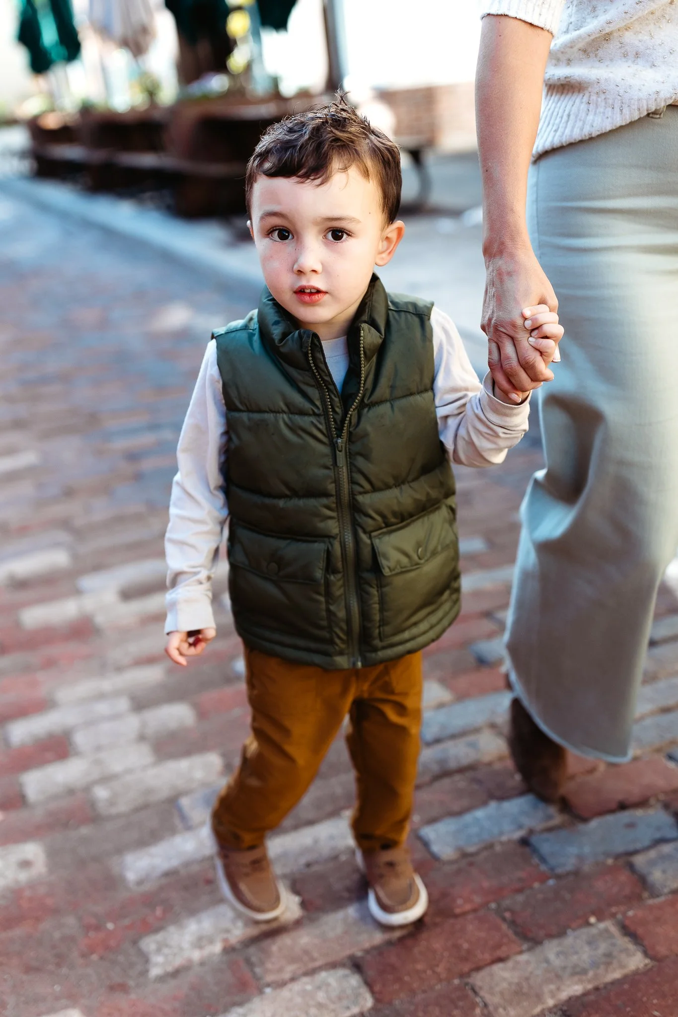 boy smiling while walking on a cobblestone street and holding mom's hand