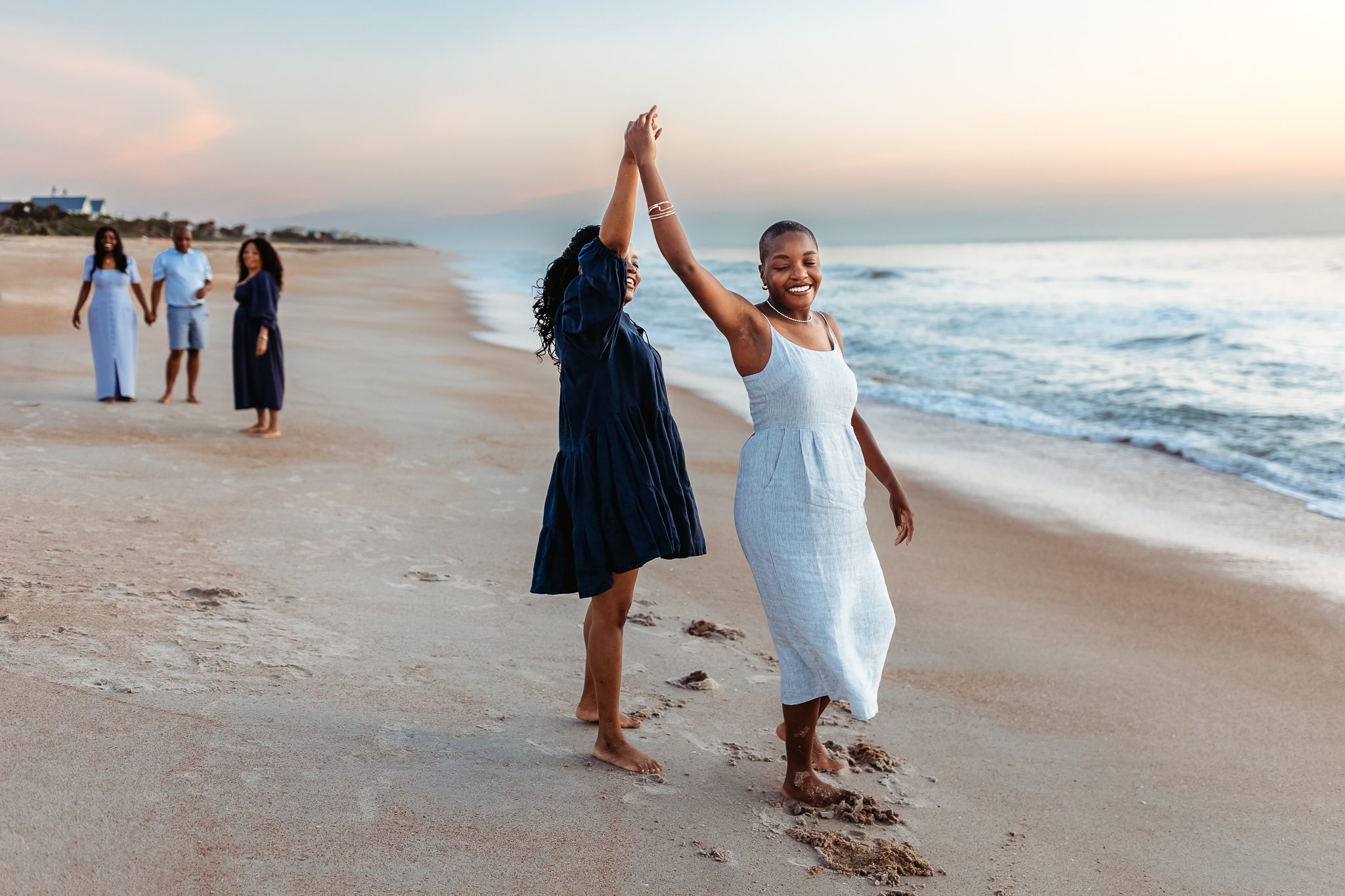 girls dancing along ocean's edge at sunrise during family photos
