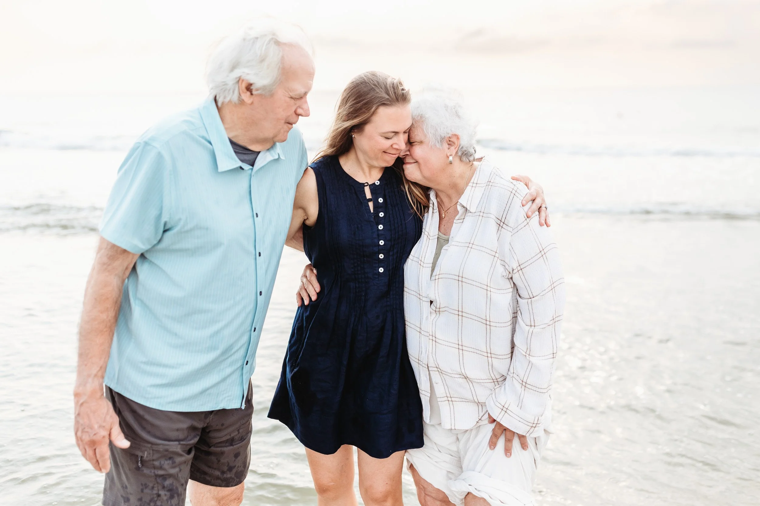 adult child being embraced by her parents on the beach at sunrise
