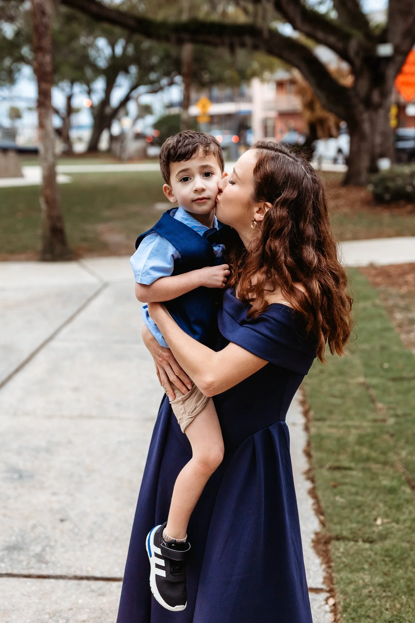 mother kissing son and holding him while he looks at camera in a courtyard