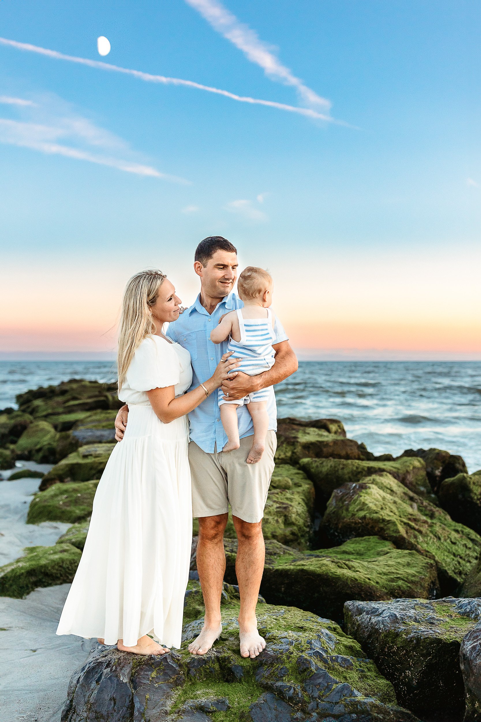 family on a jetty at sunset looking at a baby