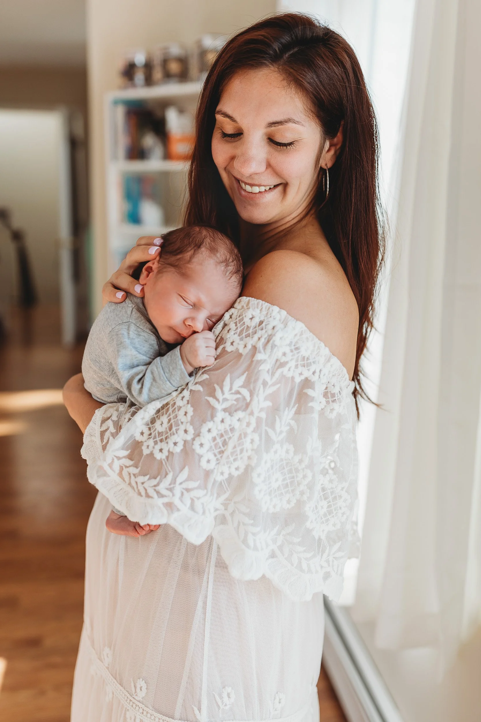 mother in ivory gown holding a sleeping baby on her shoulder and she is smiling