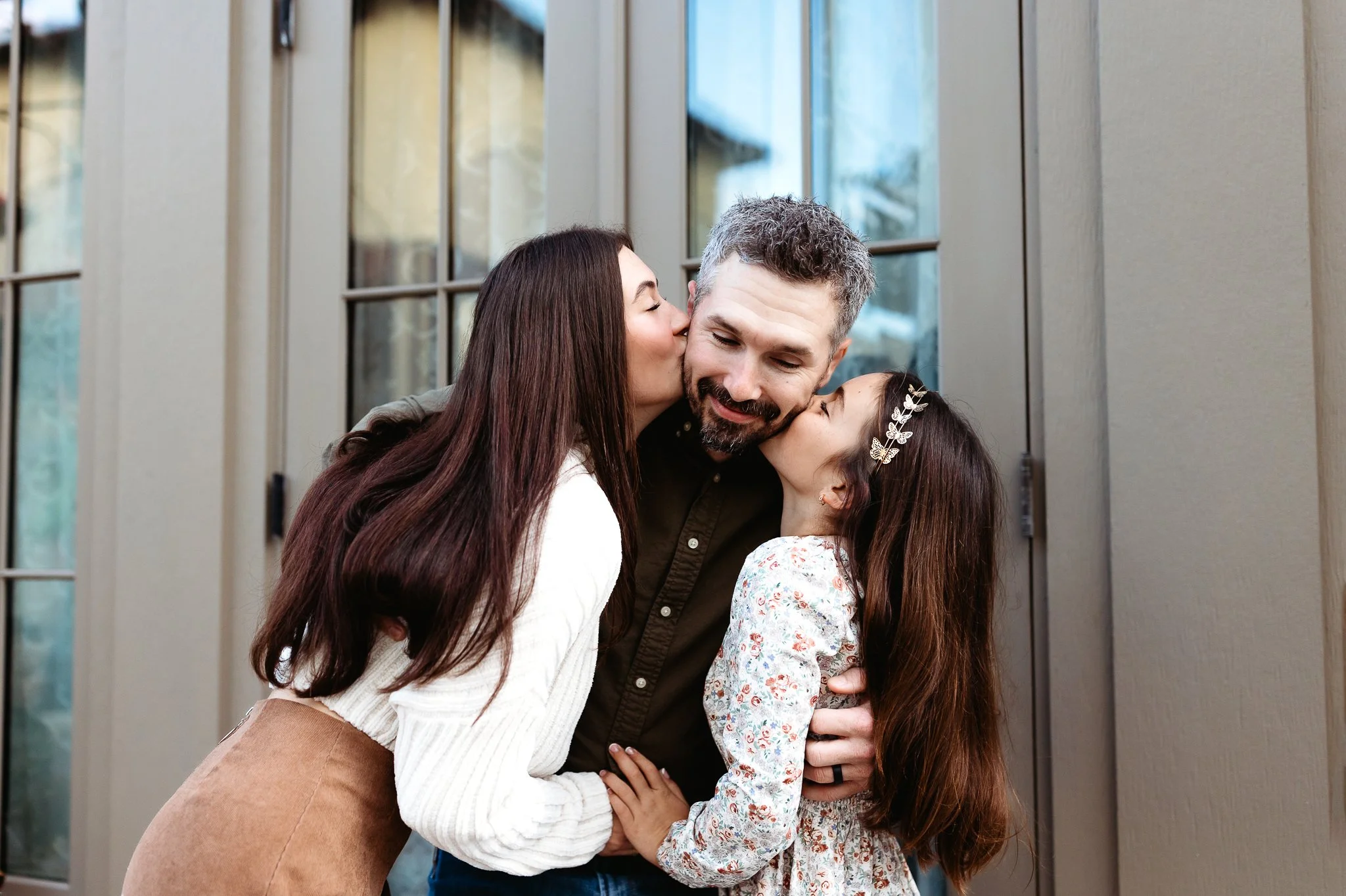 sisters kissing dad on the cheek in front of a glass door in st augustine