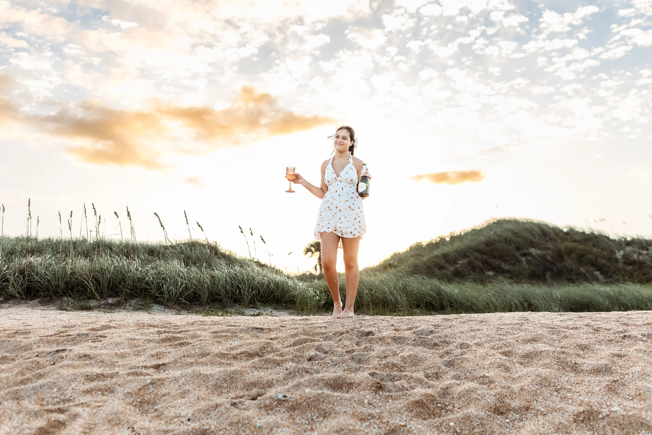 girl walking down dune at sunset with champagne and glass smiling