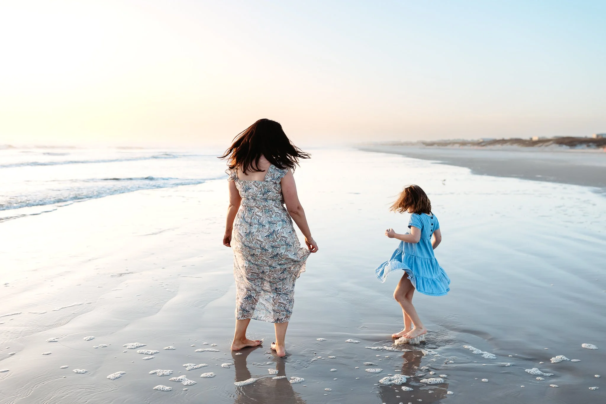 mother dancing with daughter and twirling in the ocean at sunrise during vacation family photos