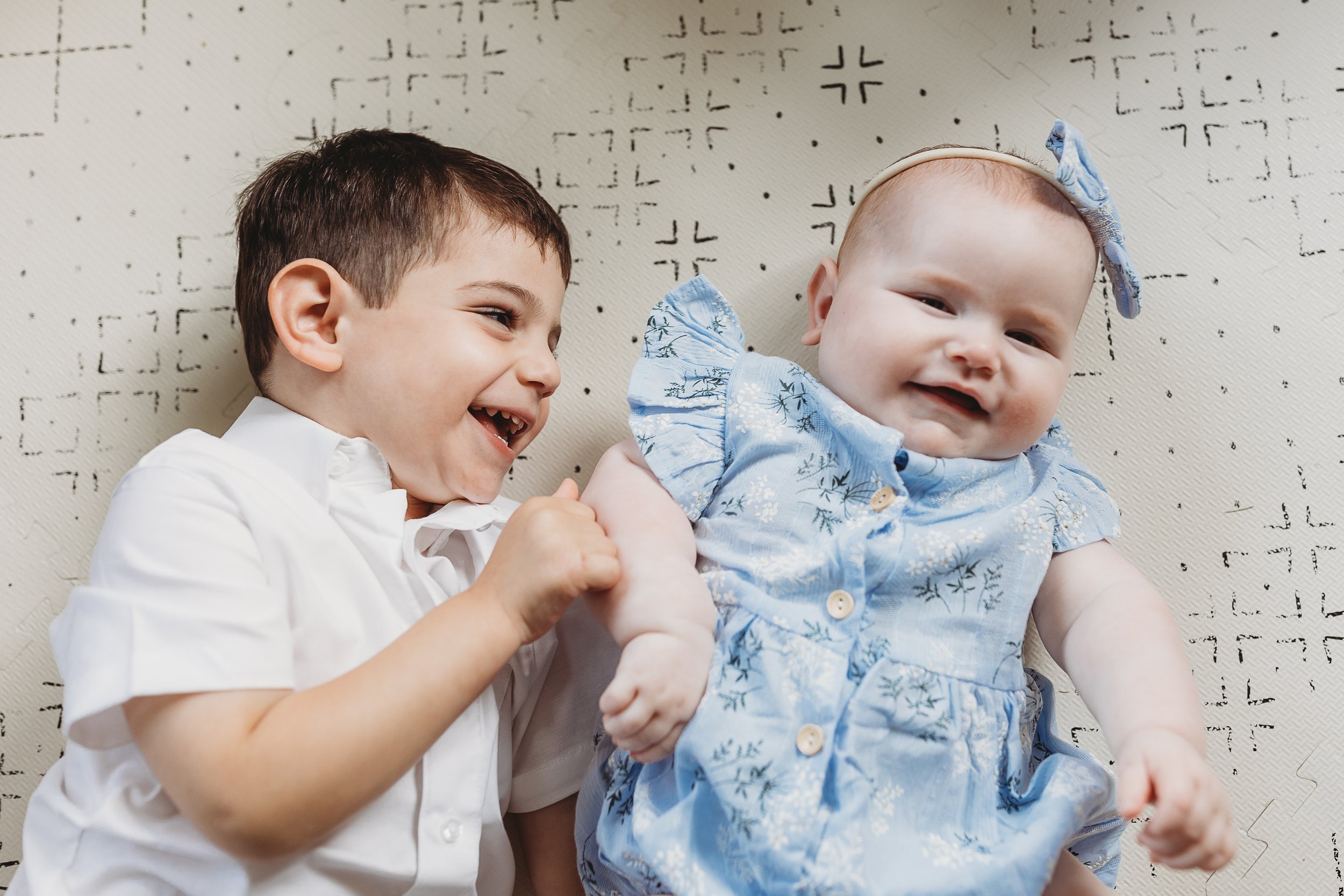 toddler and baby laying on blanket and laughing
