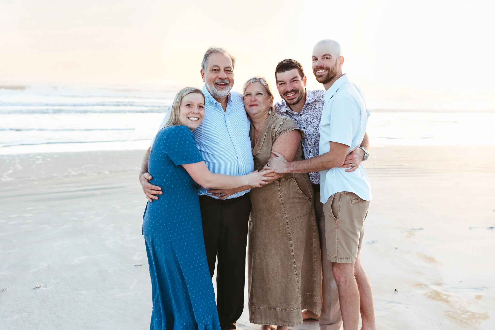 Two adult brothers and their sister smiling together during a sunrise beach family photography session.