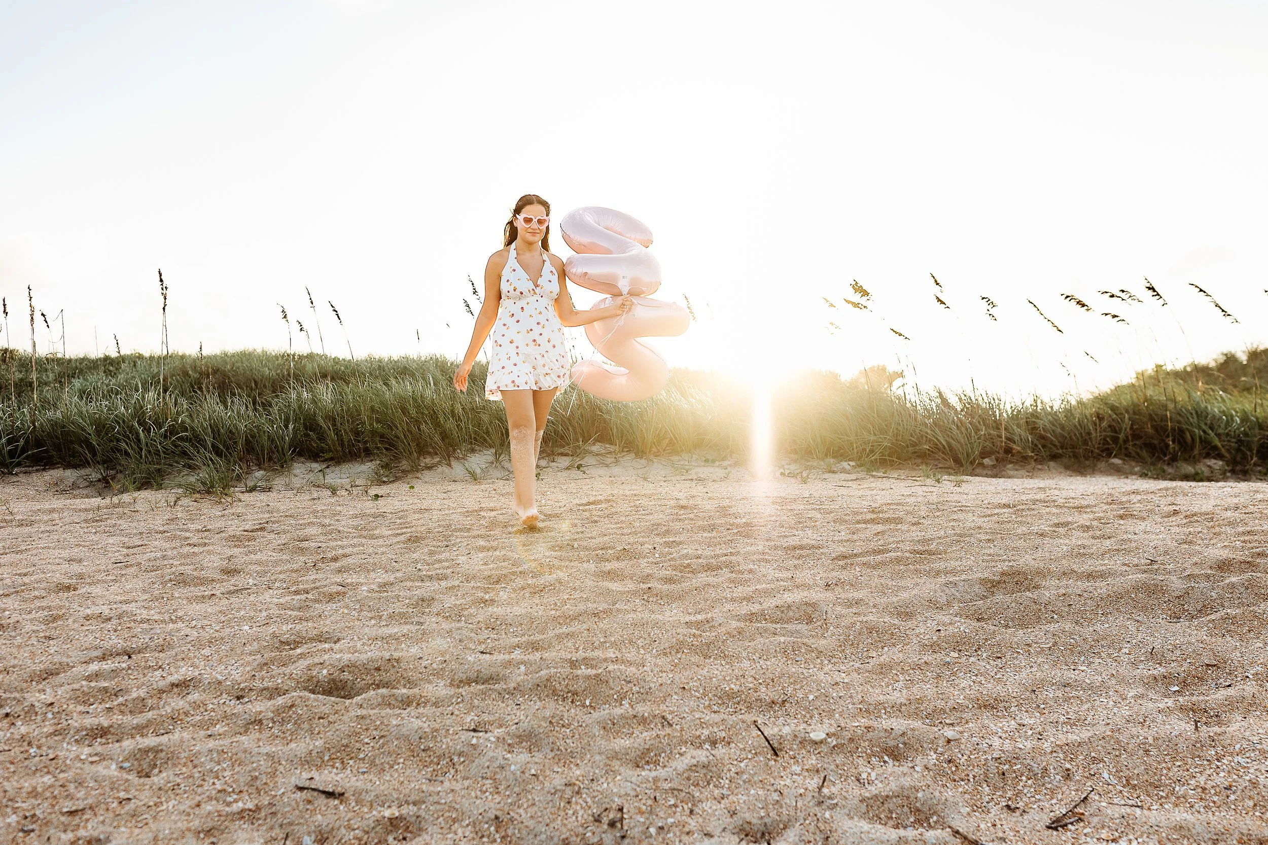 Senior portrait at golden hour with pink number balloons on a beach near Nocatee