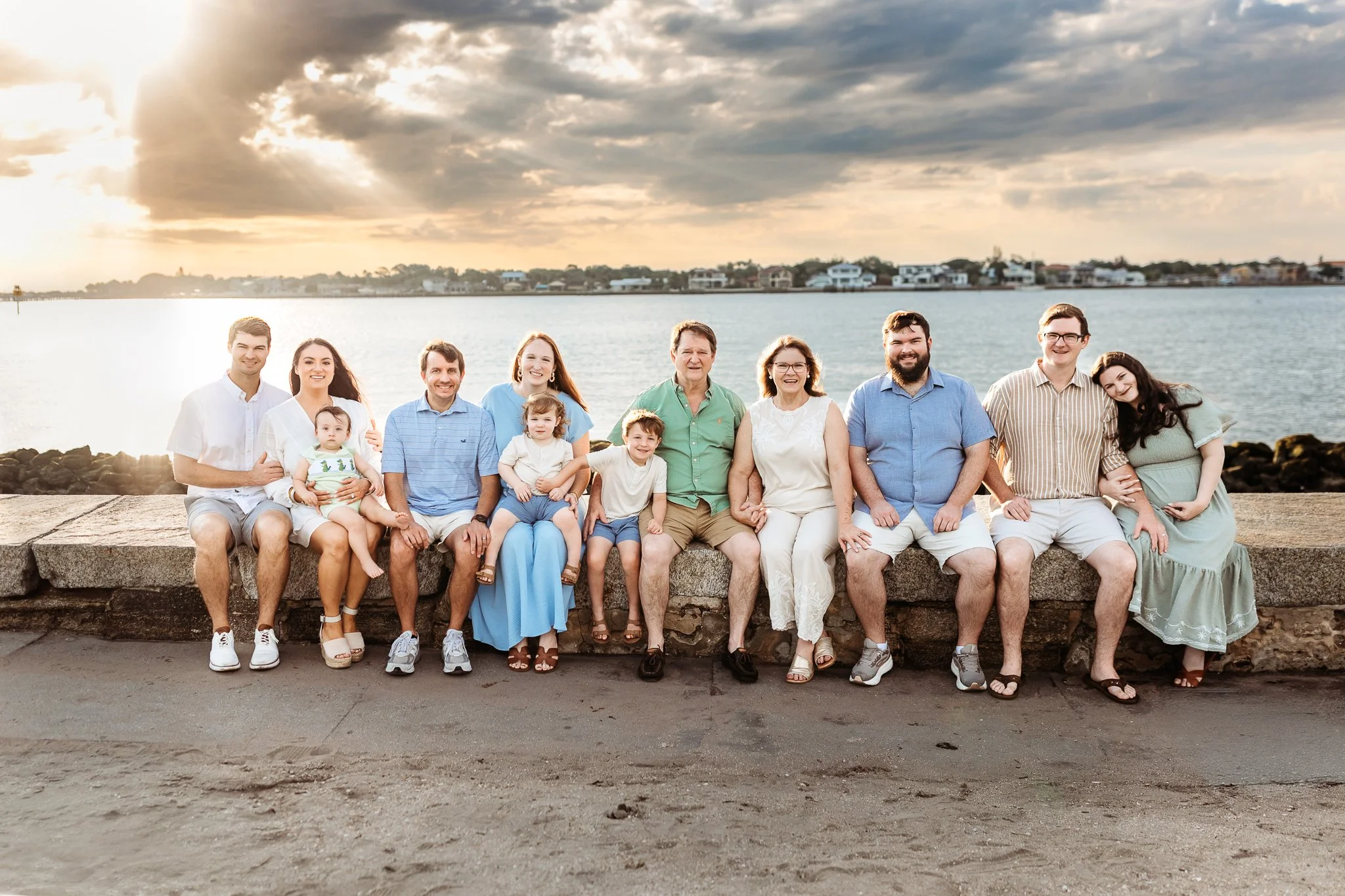 family seated on the sea wall at the Castillo de san marcos at sunrise for a family portrait and they are wearing blue and green